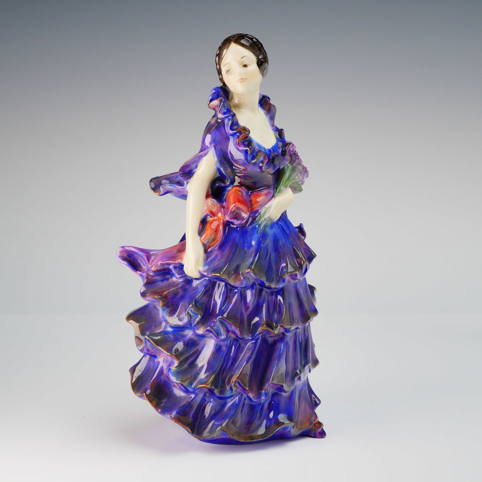 Royal Doulton Porcelain Figurine, Pamela HN1468: This figure depicts a standing woman in a dramatic, tiered dress. The decoration utilizes a glossy blue and purple glaze on the dress, providing a strong contrast to the pale skin tone and brown hair