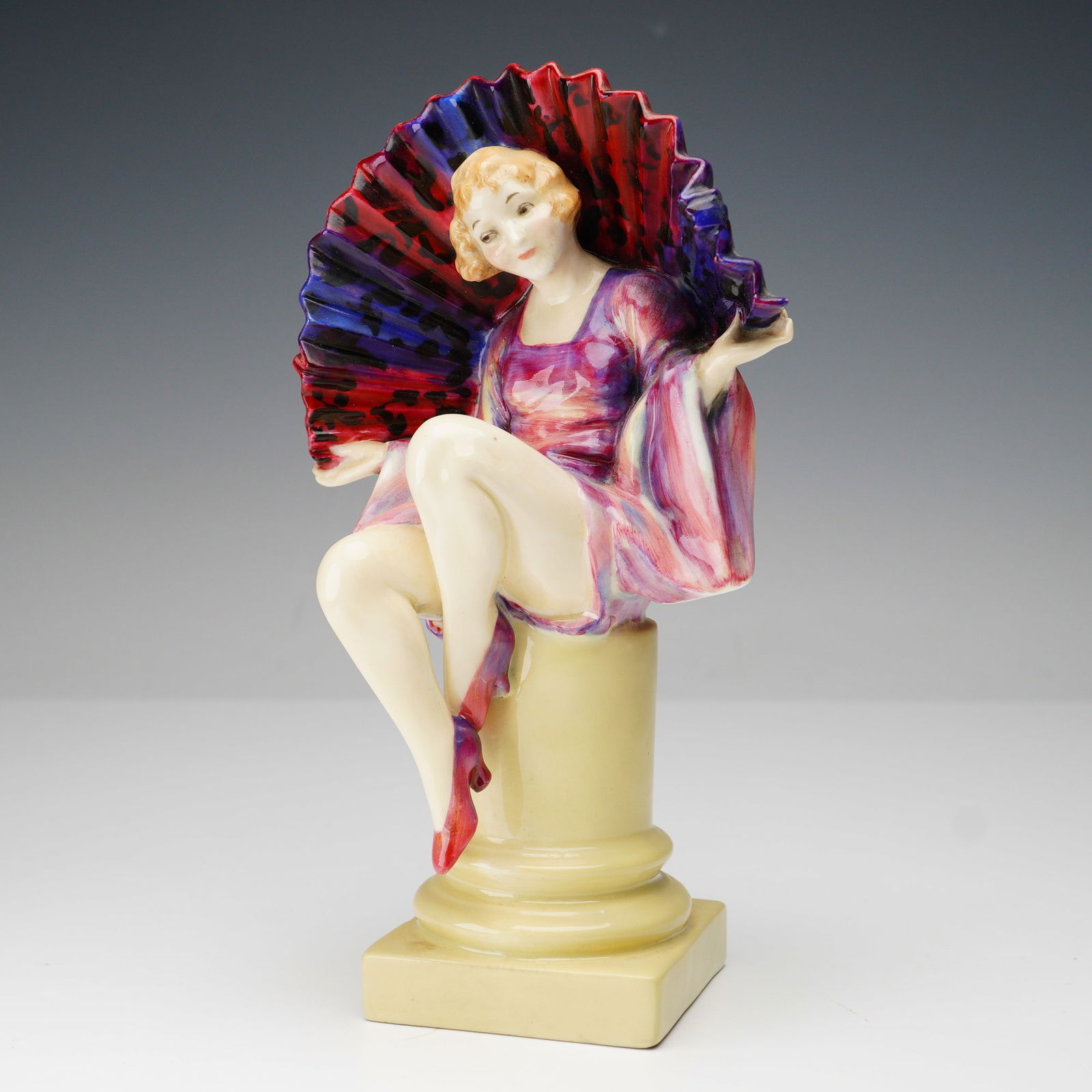 Royal Doulton Figurine, Angela HN1204: A Royal Doulton figurine titled Angela, model HN1204. This hand-painted porcelain figure depicts a seated young woman in a flowing pink and lavender dress, holding an open fan with bold red and purple