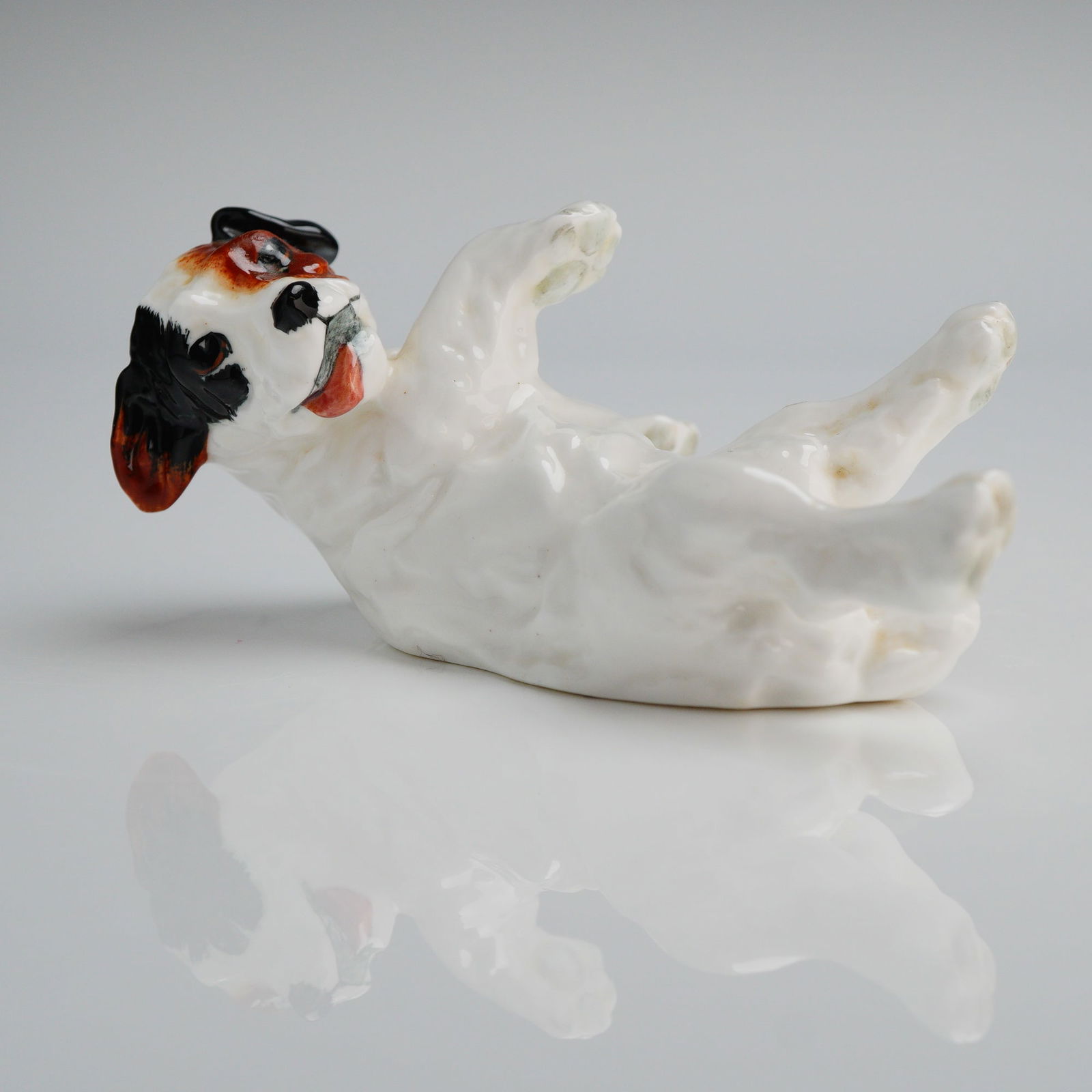 Royal Doulton Character Dog Lying on Back Figurine HN 1098: A single glazed porcelain figurine manufactured by Royal Doulton, depicting a character dog, typically identified as a Jack Russell or terrier puppy, lying on its back in a relaxed, playful posture. T