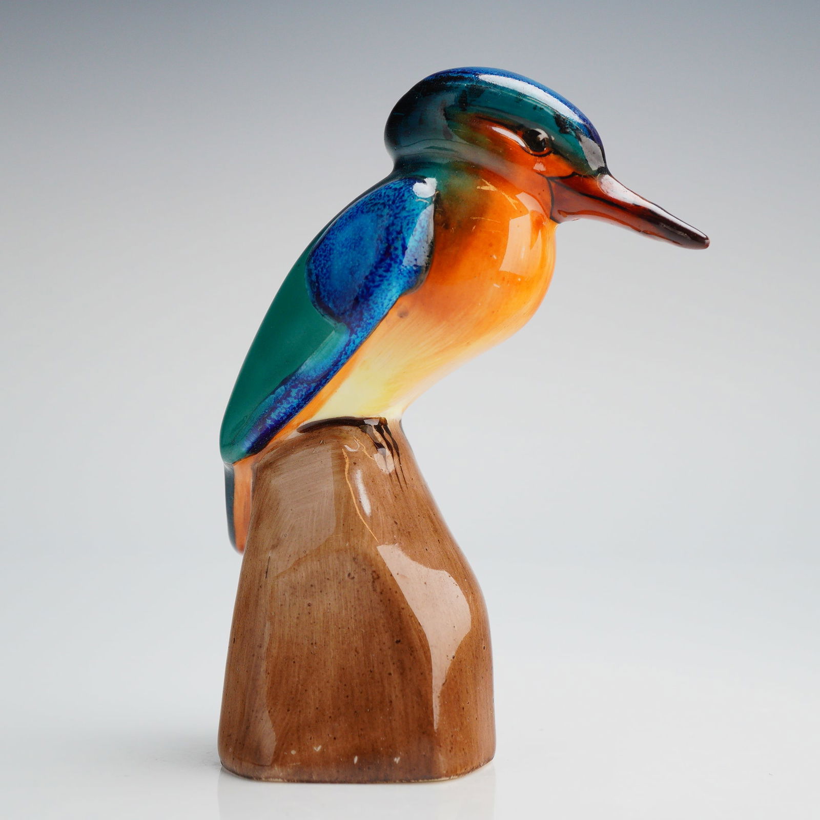 Royal Doulton Kingfisher on Rock Figurine HN131: A single ceramic figurine identified as the Royal Doulton model Kingfisher on Rock, reference number HN131. The piece is a highly glazed representation of a Kingfisher bird perched upon a brown, wood-
