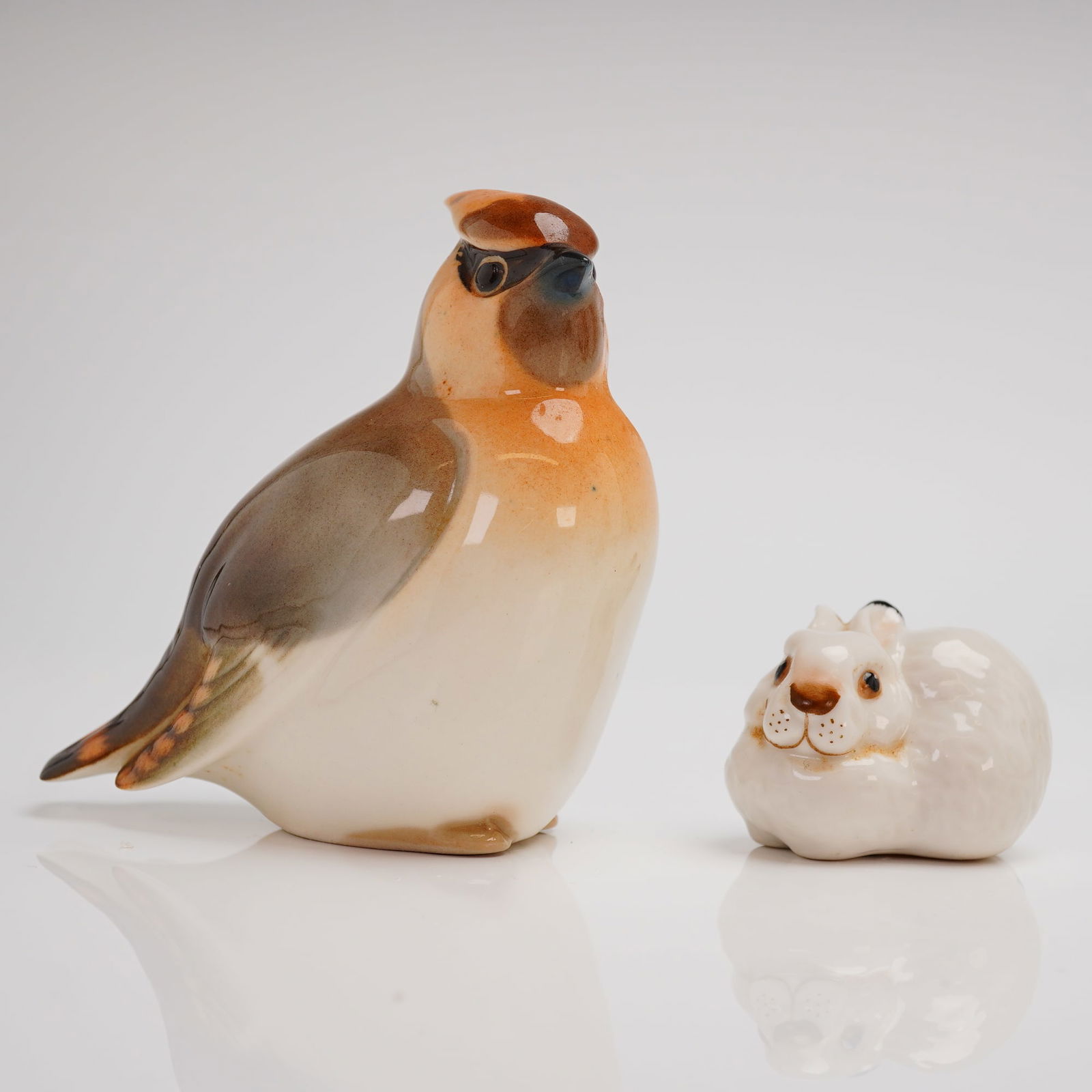 A Pair of Lomonosov USSR Porcelain Animal Figurines: A pair of Soviet Era porcelain animal figurines by Lomonosov Porcelain Factory (LFZ). The lot comprises two pieces: a larger, crested bird figurine, likely depicting a Waxwing, decorated with a high-g