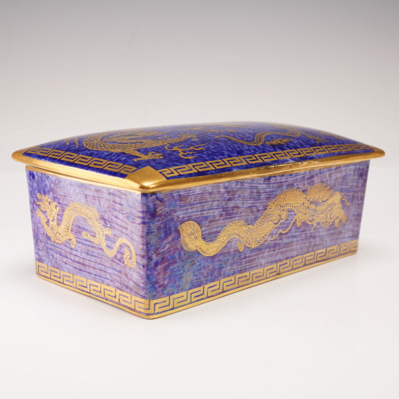 Wedgwood Fairyland Lustre Dragon Covered Box, Z4829: A rectangular ceramic box with a coordinating lid. The exterior surfaces display a mixed-blue lustre with a mottled glaze and pale coloration, and are decorated with repeating Asian dragon motifs bord