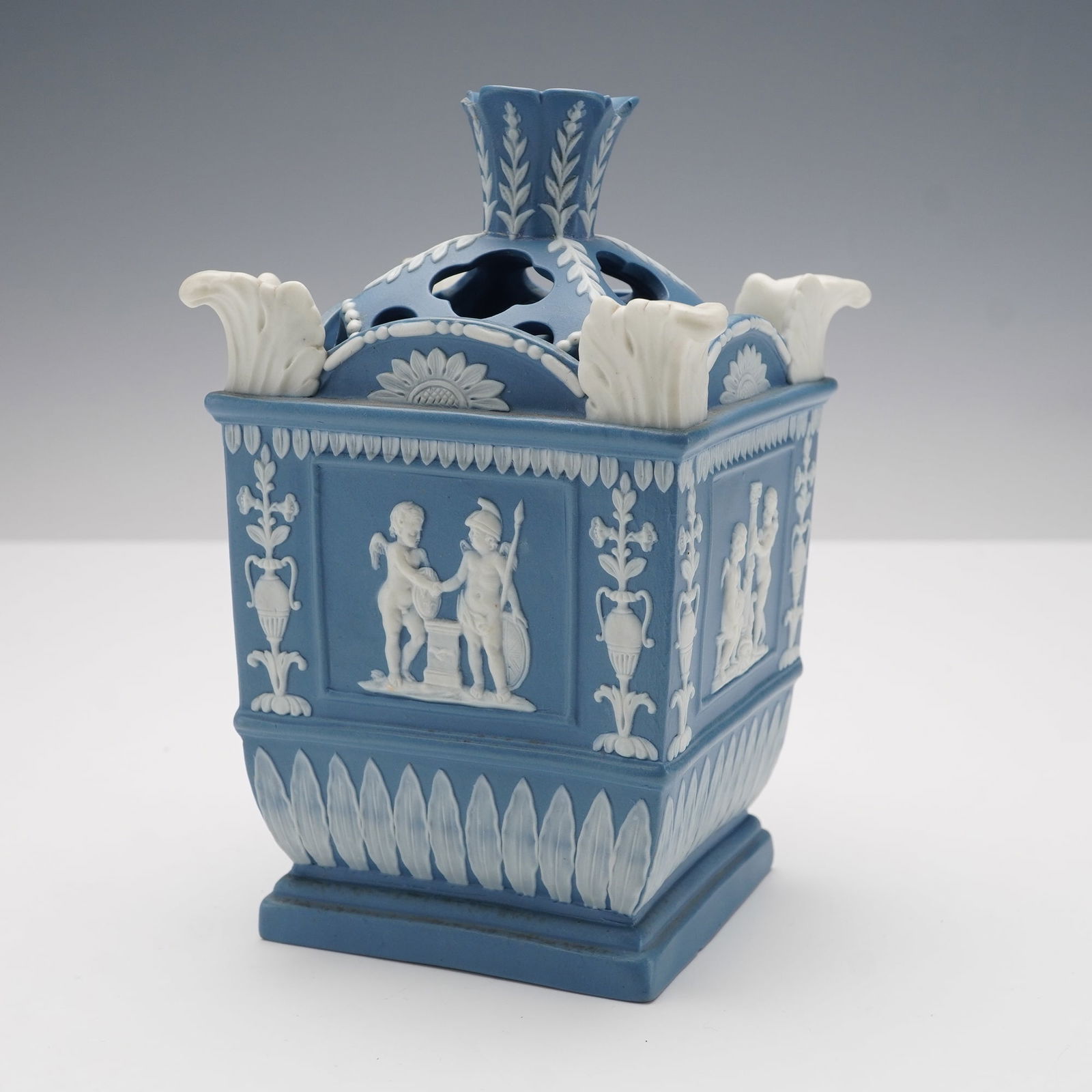 Neale and Co Blue Jasperware Flower Vase with Pierced Cover: The square form features white relief decoration on all sides depicting putti symbolizing the Anglo-French commercial treaty of 1786, representing Commerce, Art and Industry, and Liberty. Classical mo