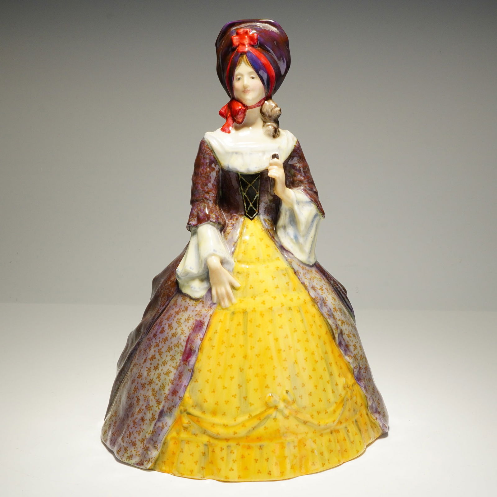 Royal Doulton Porcleain Figurine, Lady of the Georgian Period HN331: A hand-painted English porcelain figure from the Grand Dame series depicting a Georgian-period lady. Modeled wearing a purple floral-patterned dress over a yellow skirt, with a purple-and-red bonnet a