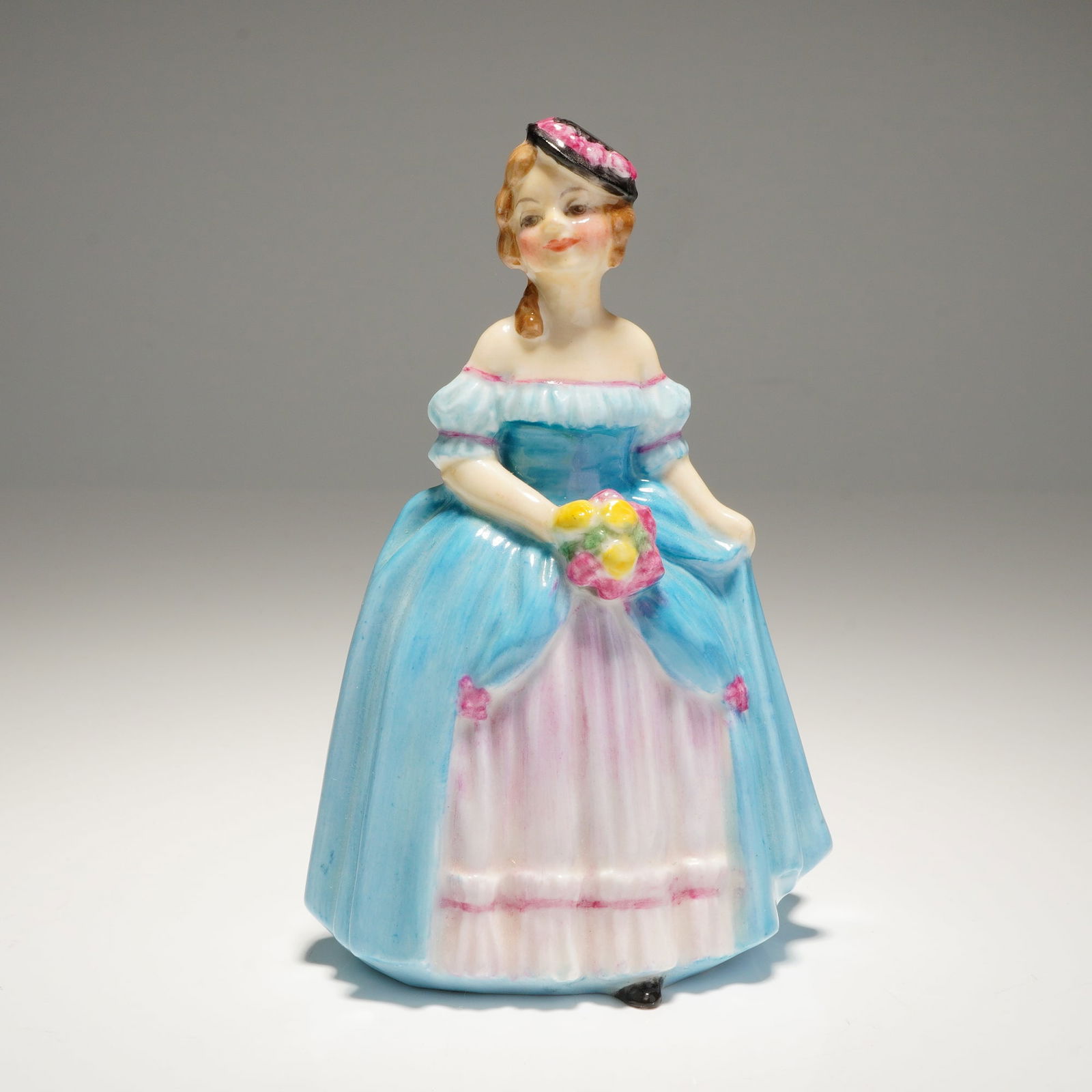 Royal Doulton Miniature Figurine Dainty May M67: A single Dainty May M67 Royal Doulton Figurine depicting a woman in a blue and pink dress holding a bouquet, marked "ROYAL DOULTON" and "MADE IN ENGLAND CHINA" on the base. Dimensions: 2.75"L x 2.00"W