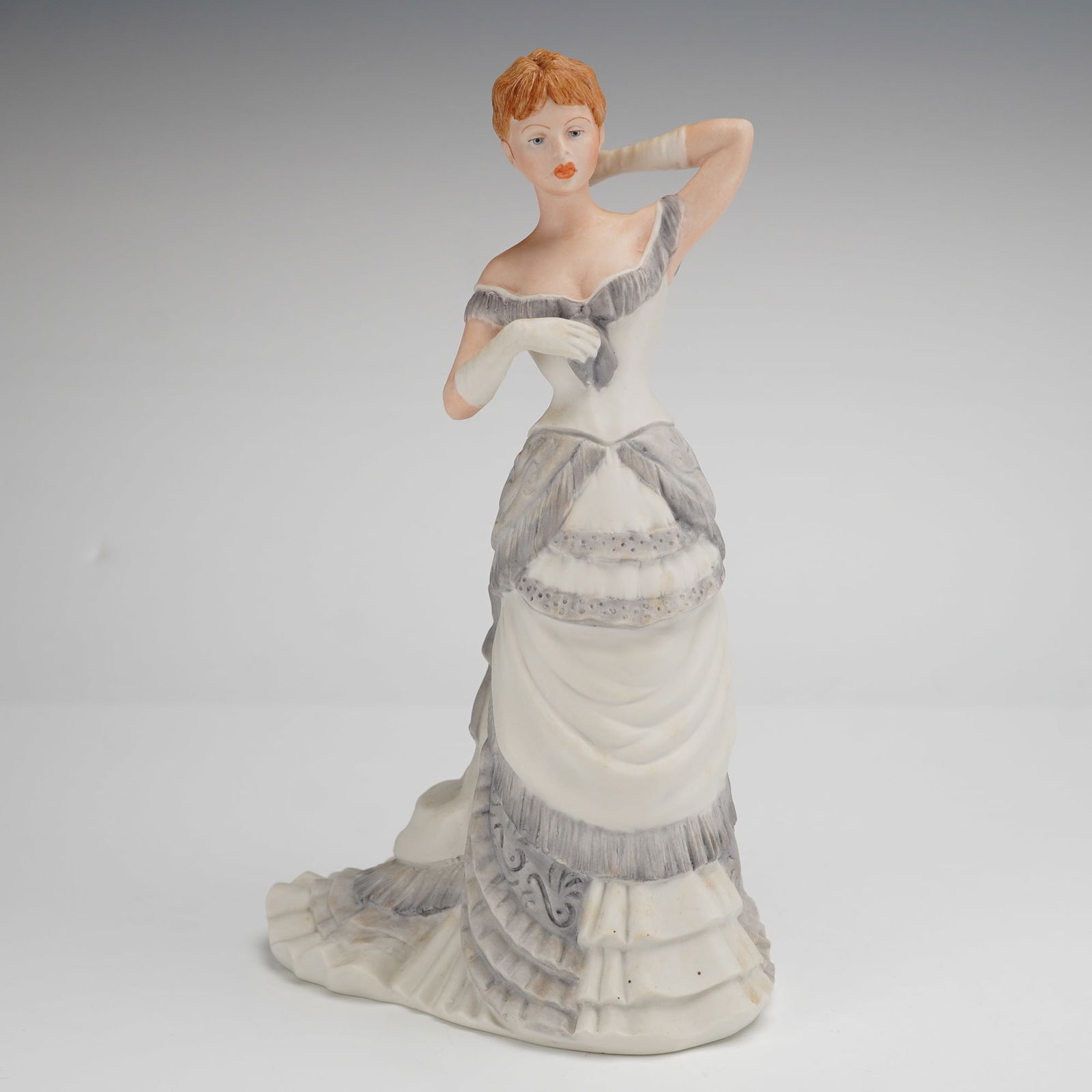 Coalport Age of Elegance Collection Figurine, Grand Parade: The figure is constructed of matte-finished porcelain and depicts a woman in a Victorian-style evening gown. The garment is primarily white with gray fringed and ruffled accents, featuring a large bus