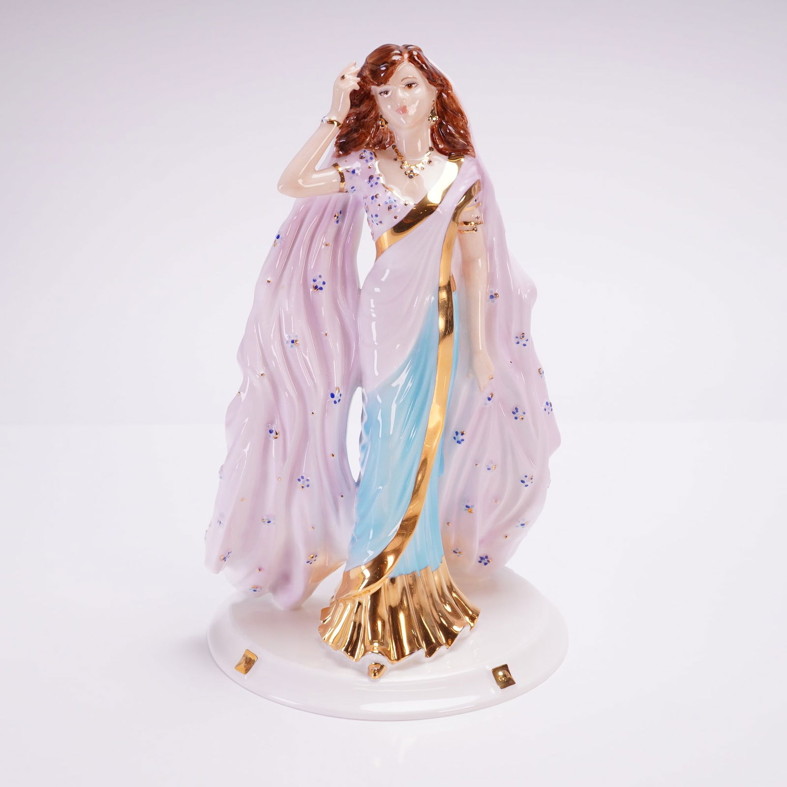 Coalport David Shilling Celebration Figurine, Sari Sensation: This hand-decorated figure depicts a standing female figure dressed in a flowing lavender and turquoise blue sari, accented with gilt trim and small floral motifs. The underside is fully marked with t