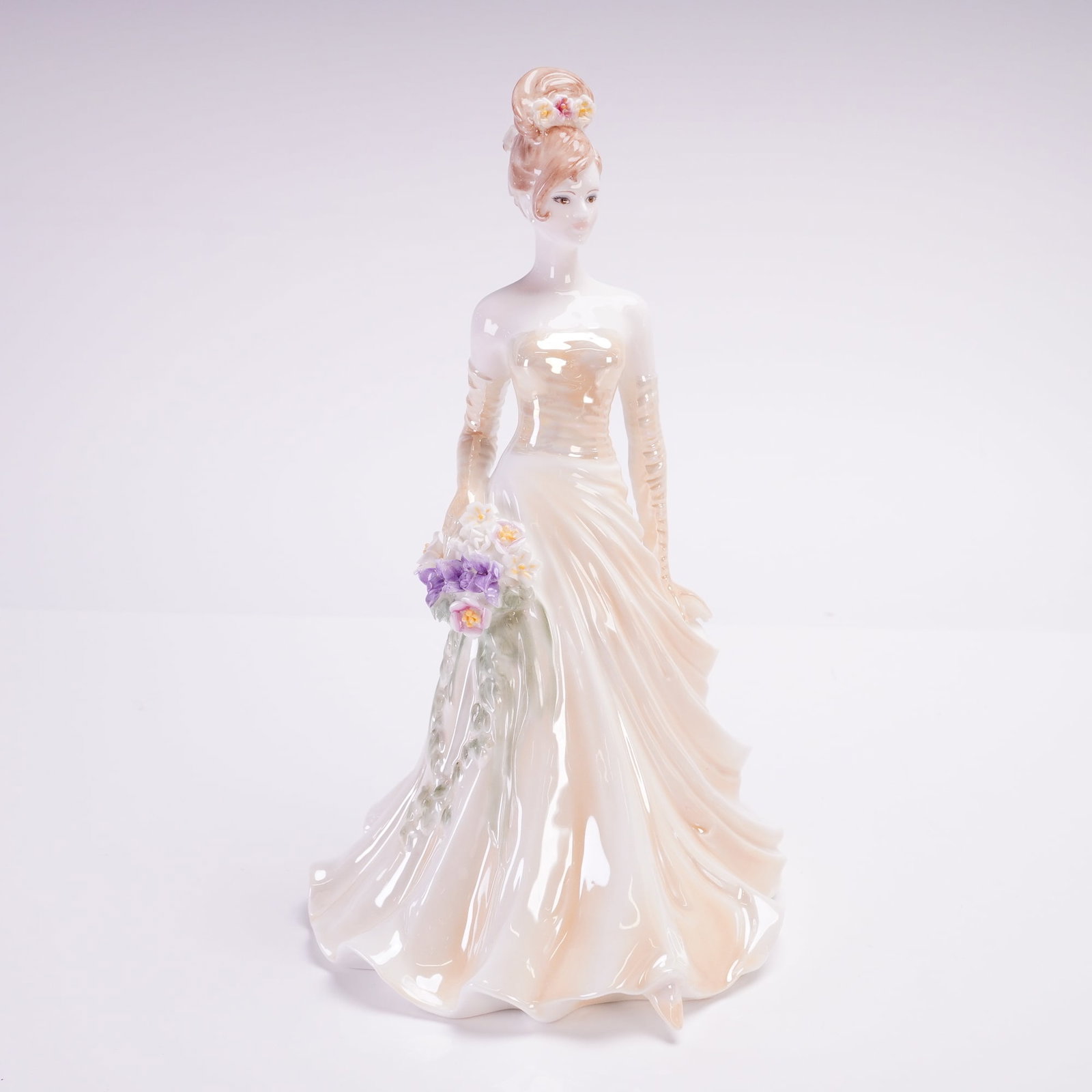 Coalport The Modern Bride Collection Figurine, Vienna: A Coalport figurine issued as a limited edition numbered 626 of 2,000. The figure is depicted wearing a strapless, pale-cream gown with a mother-of-pearl luster finish. She holds a bouquet of purple a
