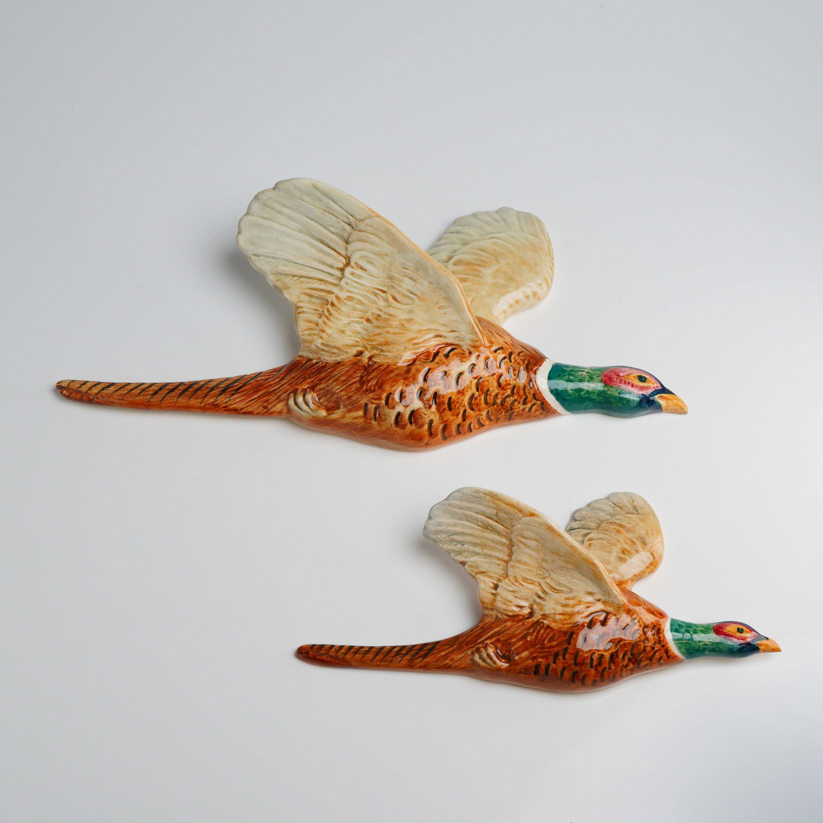 2pc Beswick Flying Pheasant Wall Plaques: A pair of graduated Beswick flying pheasant wall plaques, model numbers 661 and 661/3. These mid-century ceramic plaques are constructed from an off-white earthenware body with a glazed polychrome fin