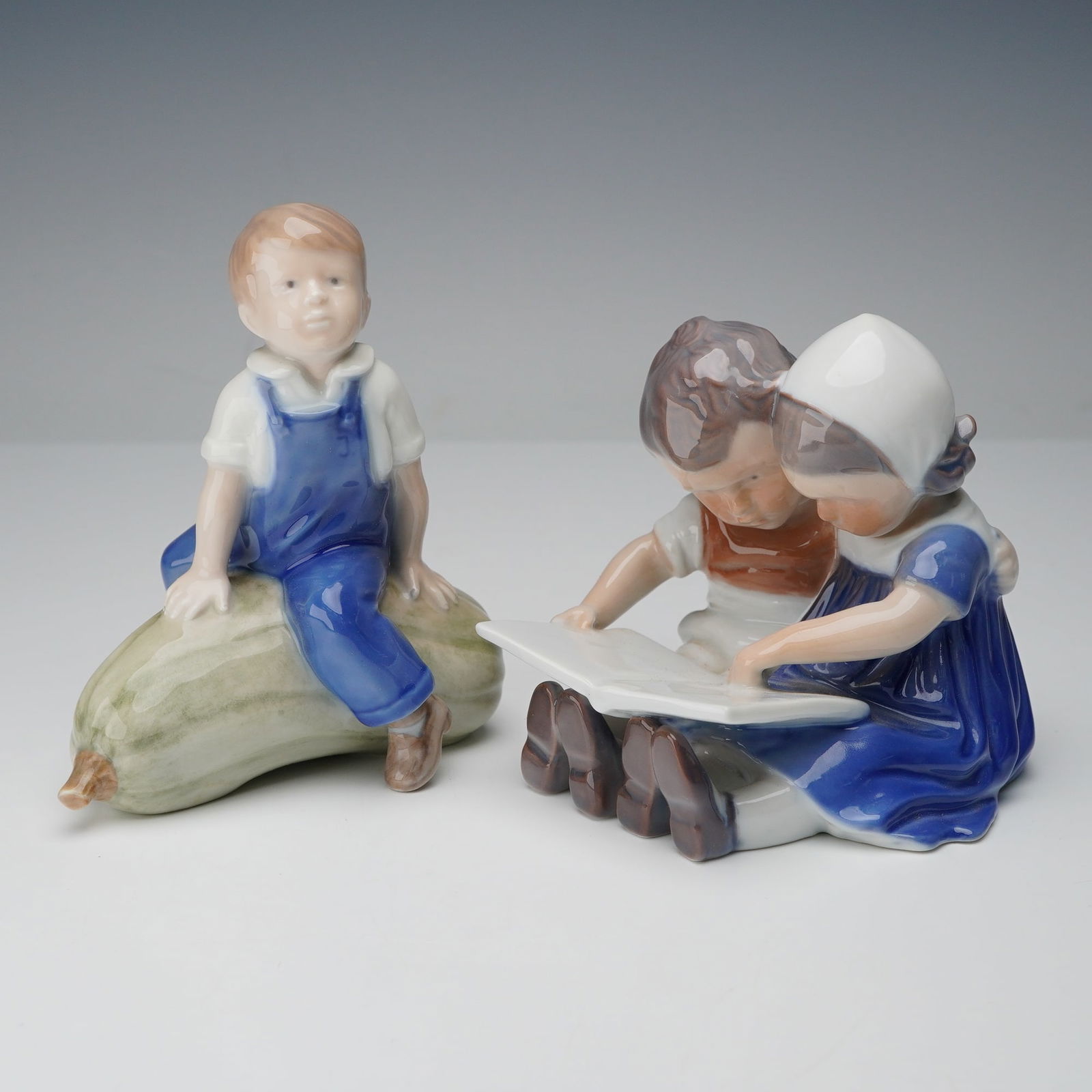 2pc Royal Copenhagen and Bing & Grondahl Children Figurines: Collection includes a Royal Copenhagen porcelain figurine (no. 4539) depicting a boy seated on a large gourd with both hands resting on it, underside marked with the Royal Copenhagen hallmark and mode