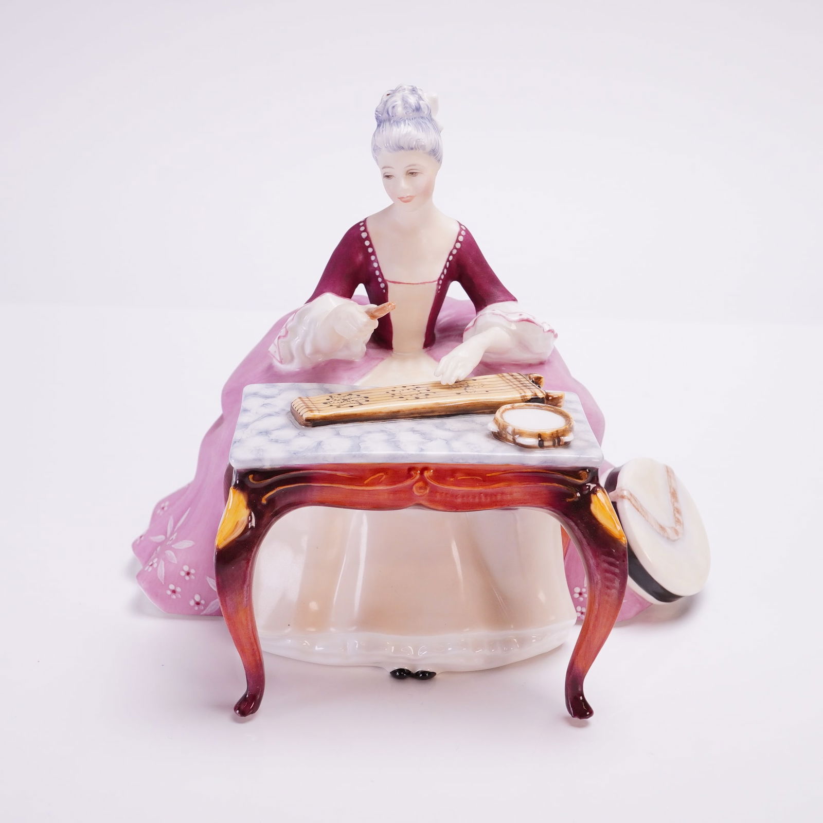 Royal Doulton Figurine, Dulcimer HN2798: A Royal Doulton bone china figurine is from the Lady Musician series. Modeled by Peggy Davies, the piece depicts a female figure in 18th-century style dress, featuring a maroon bodice and a pink skirt