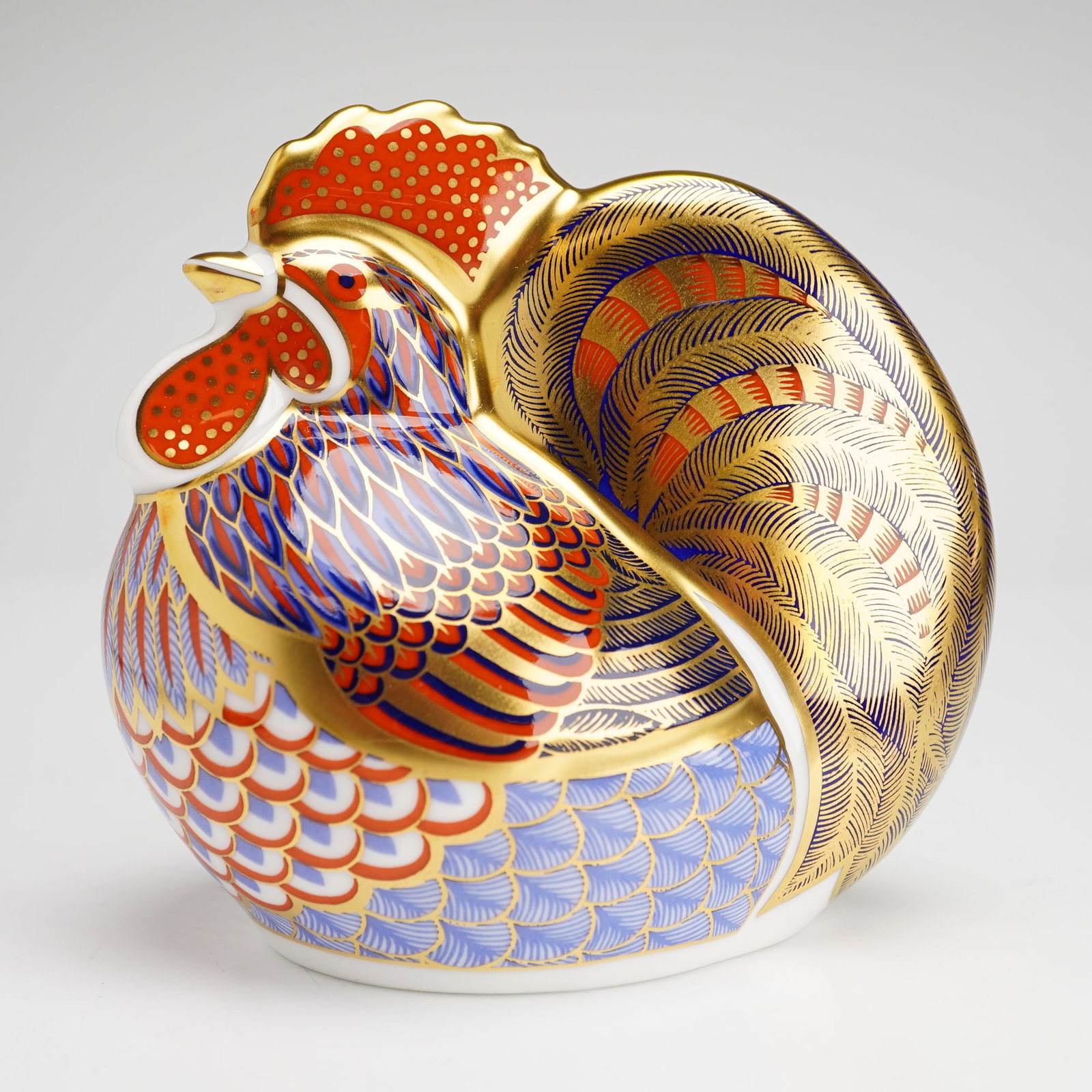 Royal Crown Derby Paperweight, Cockerel: The piece is decorated in the traditional Imari palette, featuring cobalt blue and iron red underglaze with extensive gold gilding. The design includes intricate feather-like patterns across the body