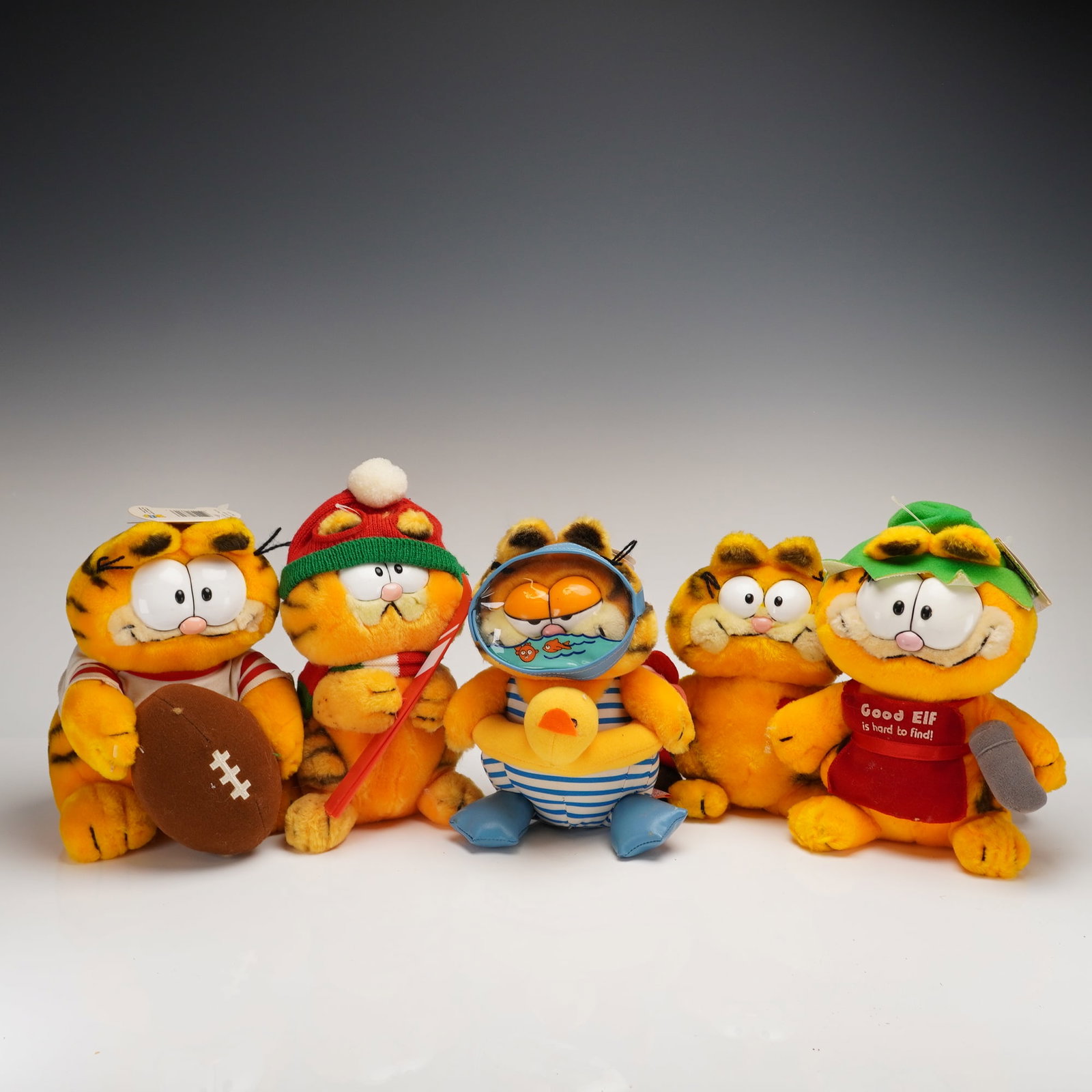 A Collection of 5 Vintage Dakin Garfield Plush Toys: A collection of 5 vintage Garfield plush toys produced by R. Dakin & Company. The figures are constructed from synthetic orange and black striped fabric. Each figure depicts the iconic tabby cat in va