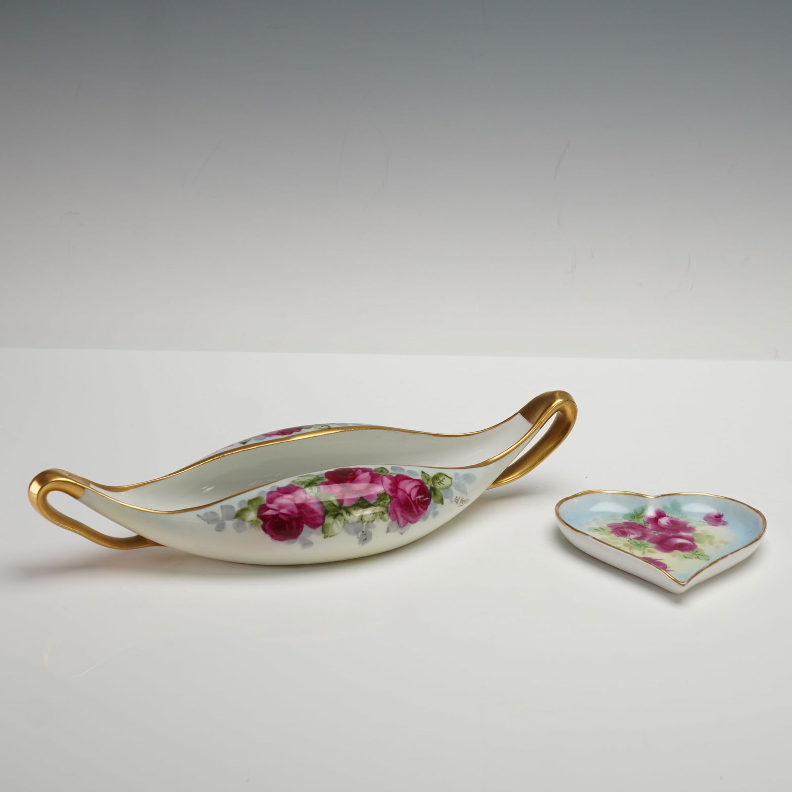 2pc Hand Painted Austrian & Bavaria Floral Dishes: Includes an elegant Austrian hand-painted dish featuring vibrant red roses by artist Ed Heyn, alongside a heart-shaped dish adorned with red roses by William Wands, marked Bavaria. The elongated oval