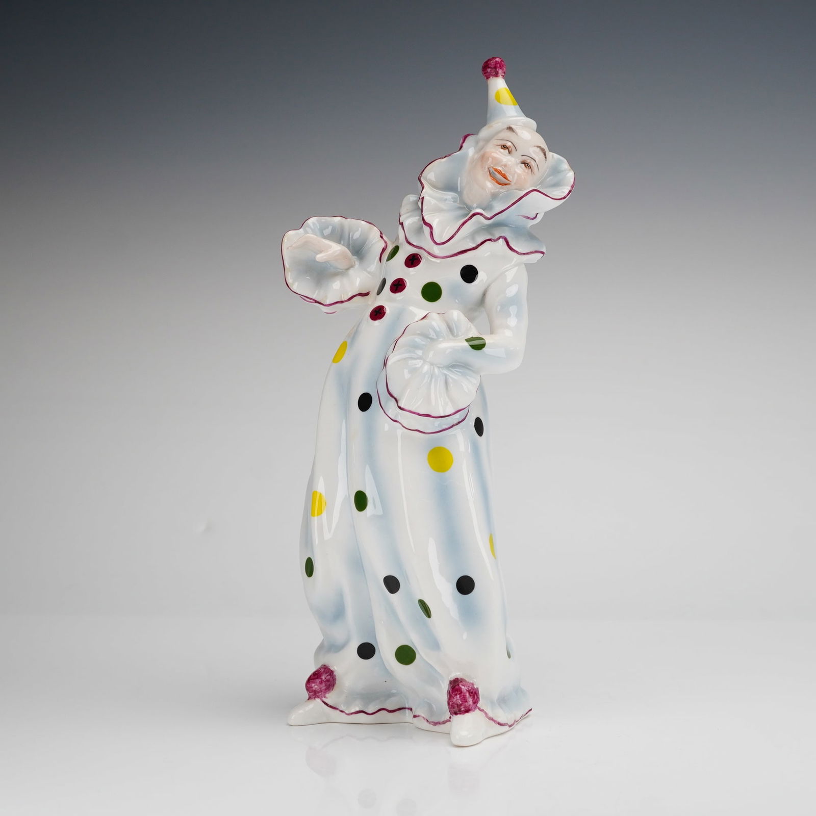 Coalport Bone China Figurine, Clown: A Coalport bone china figurine depicting a clown in a dynamic pose. The figure wears a white costume decorated with multicolored polka dots and purple-edged ruffles at the neck and cuffs. The piece fe