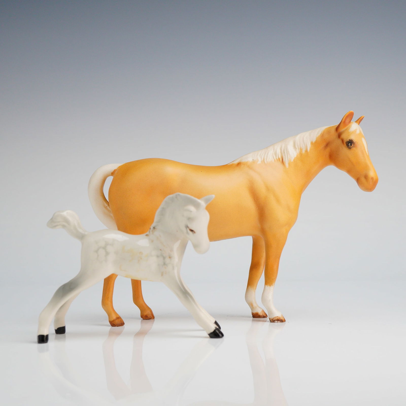 2pc Beswick Porcelain Horse Figurines: A pair of Beswick ceramic horse figurines comprising a larger palomino mare and a smaller dapple-gray foal. The mare is modeled with a matte finish, featuring a light golden-brown coat with a white ma