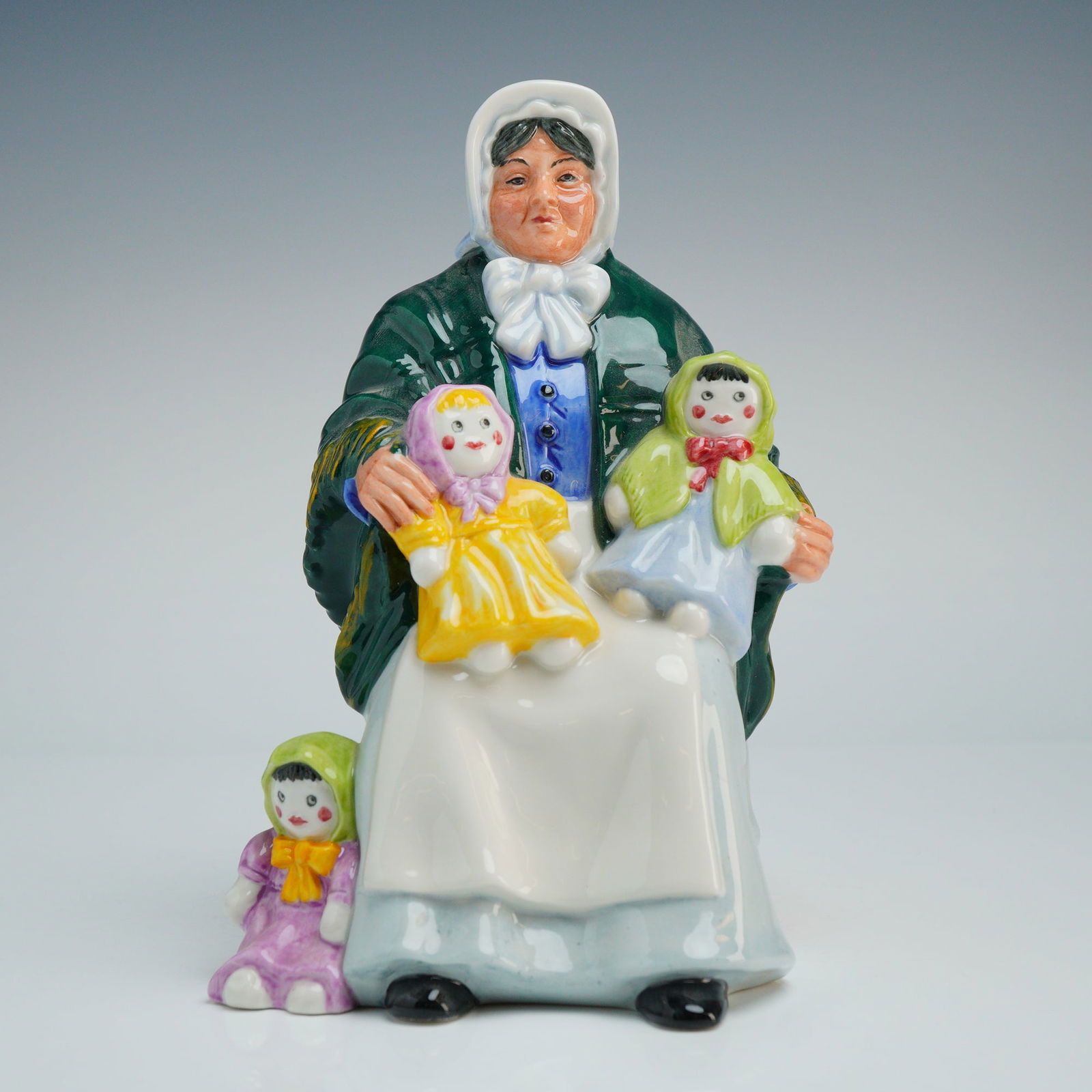 Royal Doulton Figurine, Rag Doll Seller HN2944: This hand-decorated piece was modeled by Robert J. Tabbenor and depicts an elderly woman seated on a woven wicker basket. The figure is dressed in a white bonnet, a deep green shawl with yellow fringe