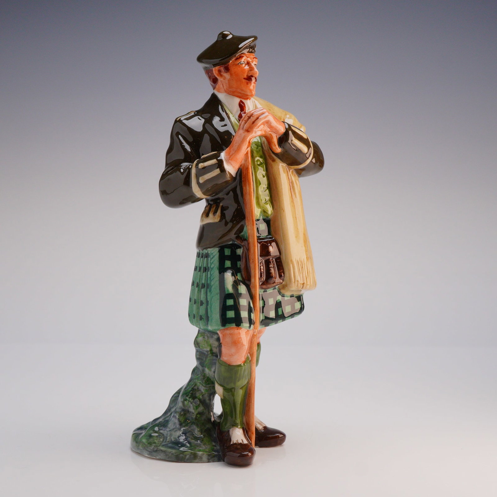 Royal Doulton Figurine The Laird HN2361: The figure is polychrome glazed, depicting a standing male figure in traditional Scottish attire, including a green tartan kilt, bonnet, sporran, and brown jacket, leaning upon a walking staff. The un
