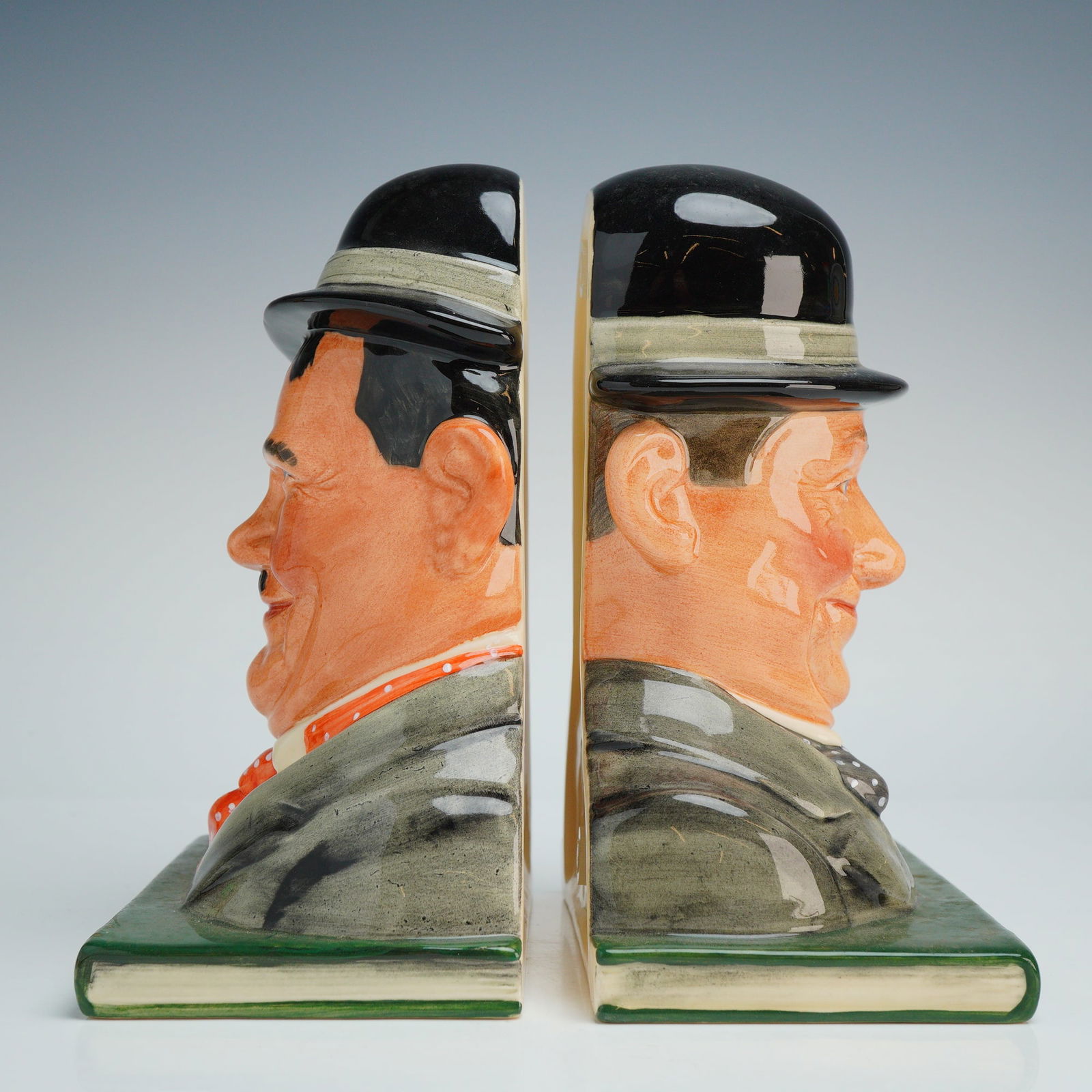 2pc Royal Doulton Bookends, Laurel and Hardy D7119, D7120: A pair of Royal Doulton hand-painted ceramic bookends featuring character busts of the comedy duo Laurel and Hardy. Modeled by William K. Harper, the figures are presented with a glossy finish atop gr