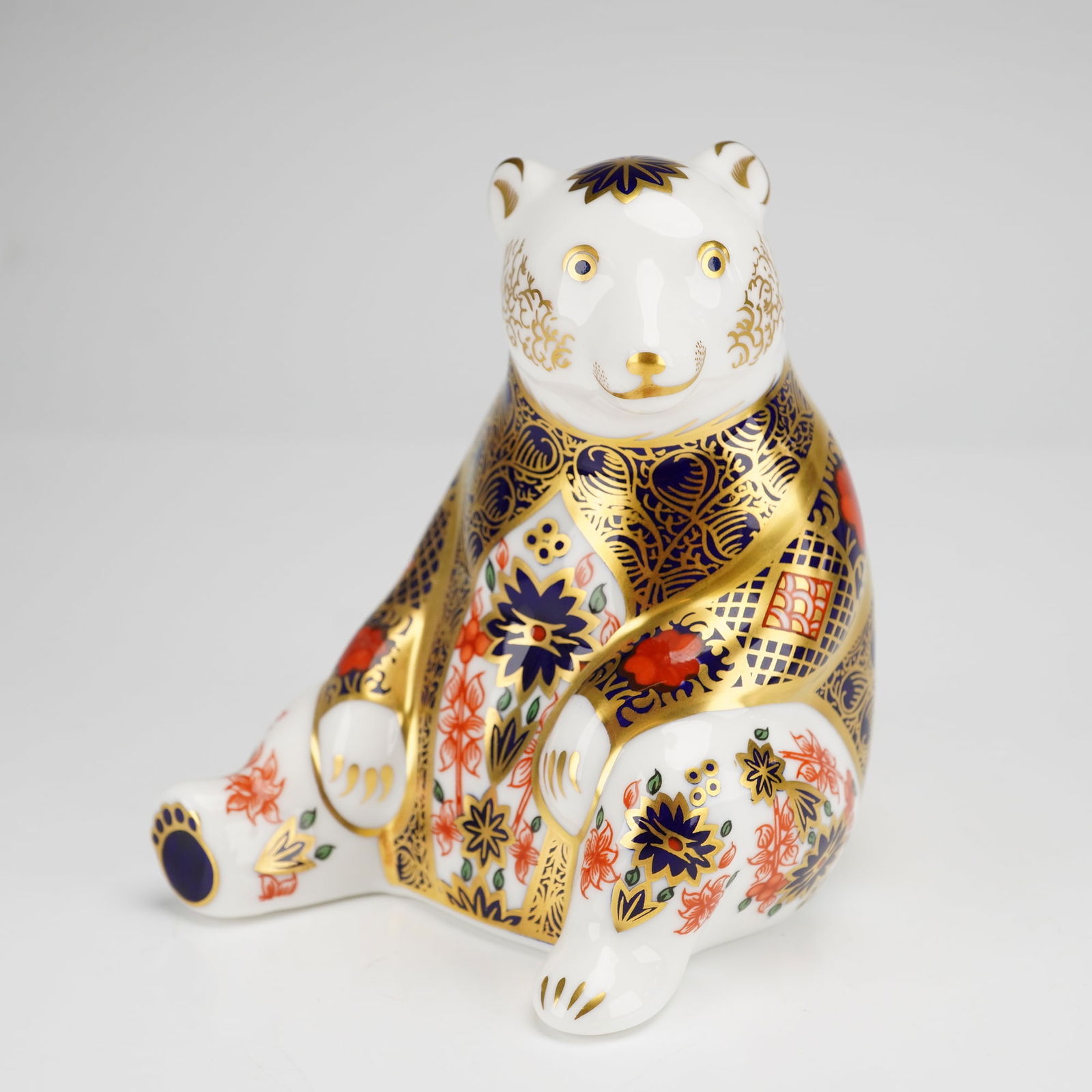 Royal Crown Derby Paperweight, Old Imari Honey Bear: This figurine depicts a sitting bear decorated in a traditional Imari palette of cobalt blue, iron red, and extensive gold gilding. The surface features floral and geometric patterns, with stylized fa