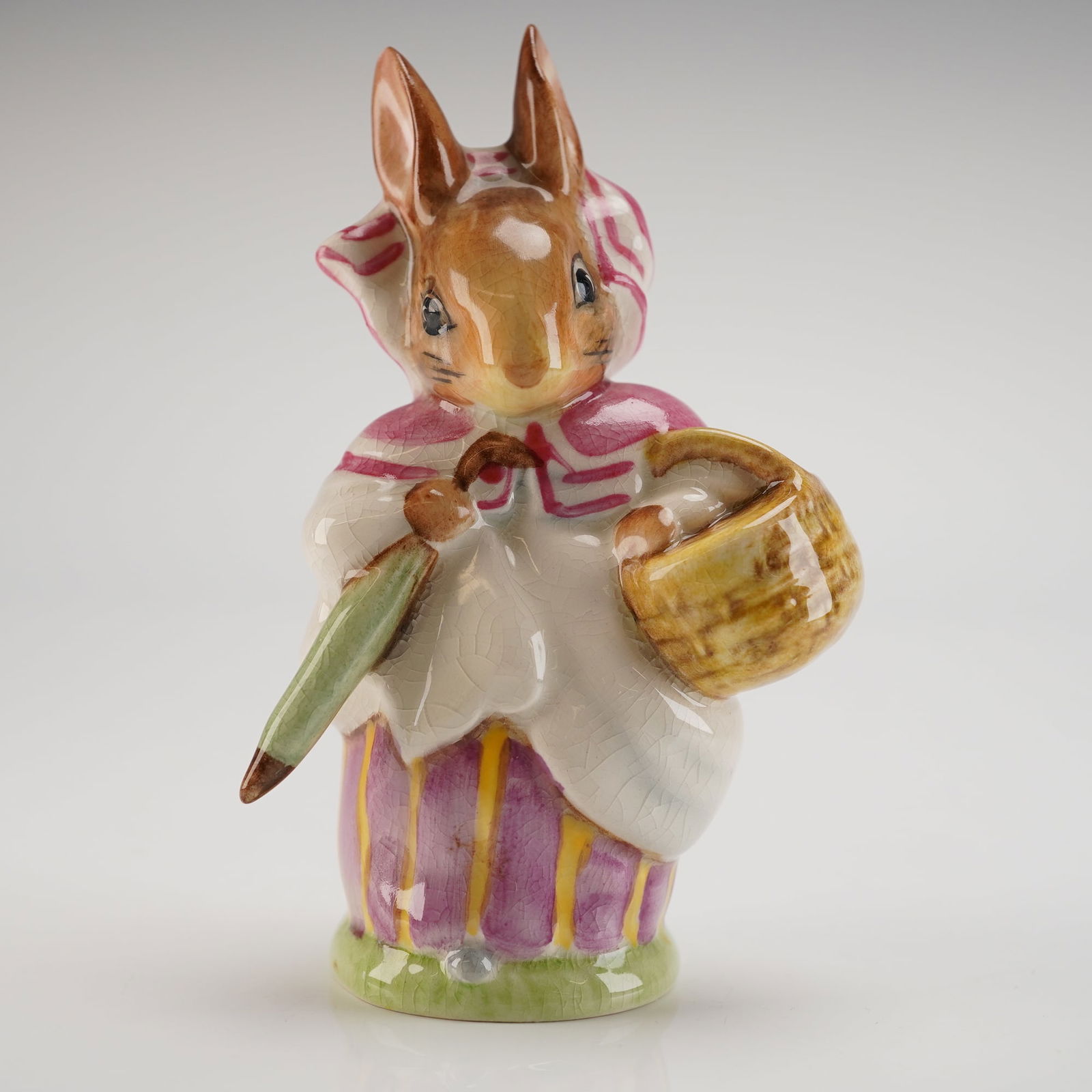 Beswick Beatrix Potter's Figurine, Mrs. Rabbit - Umbrella Out: Designed by Arthur Gredington. Depicts a brown rabbit wearing a yellow striped dress, holding a green umbrella. Features the golden Beswick oval backstamp on the underside. Model number P1200/1. Dimen