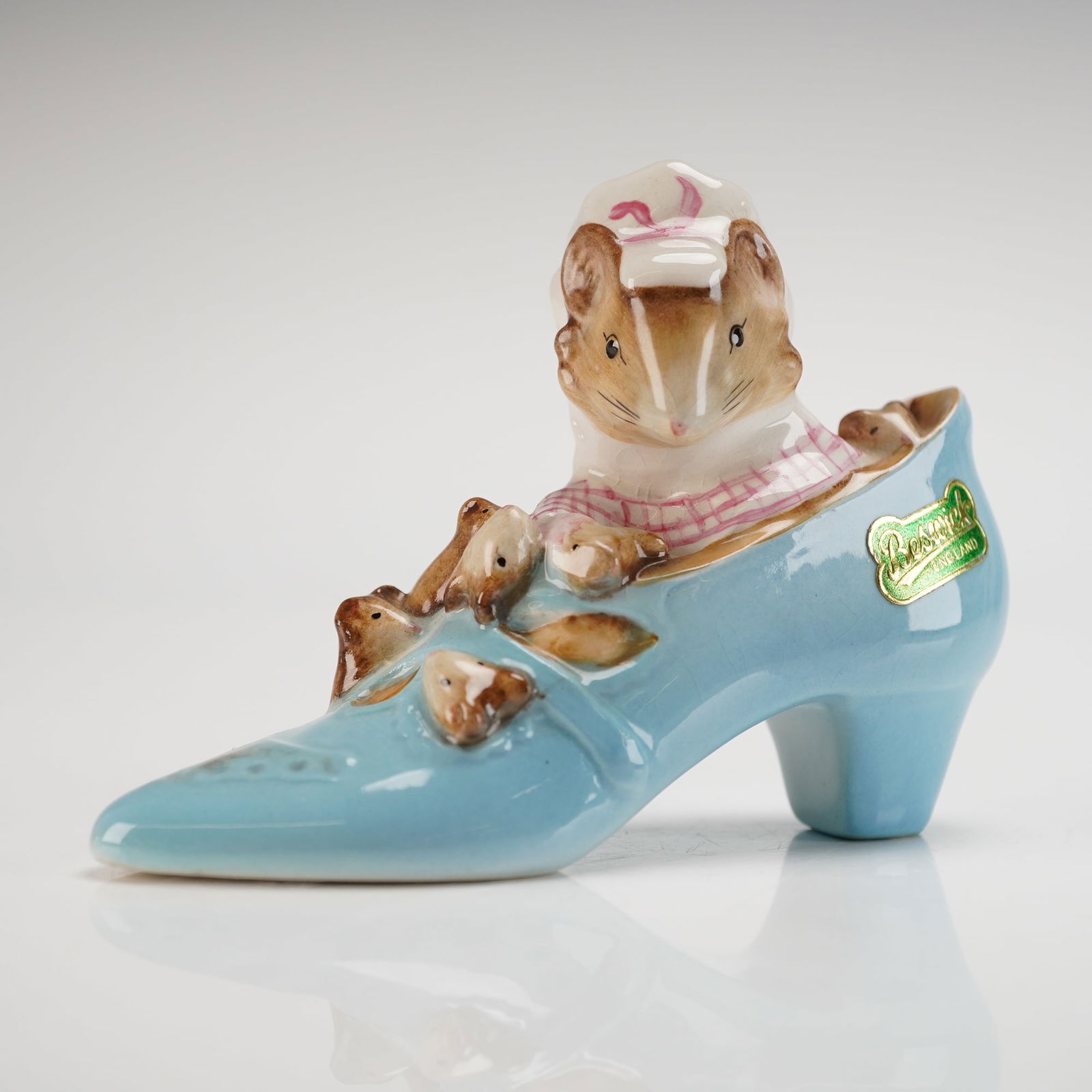 Beswick Beatrix Potter's Figurine, The Old Woman Who Lived in a Shoe: Model number P1545, showing a family of mice nestled in a blue shoe. The mother mouse wears a pink-and-white bonnet and apron, while her children peek out from around her. The side of the shoe display