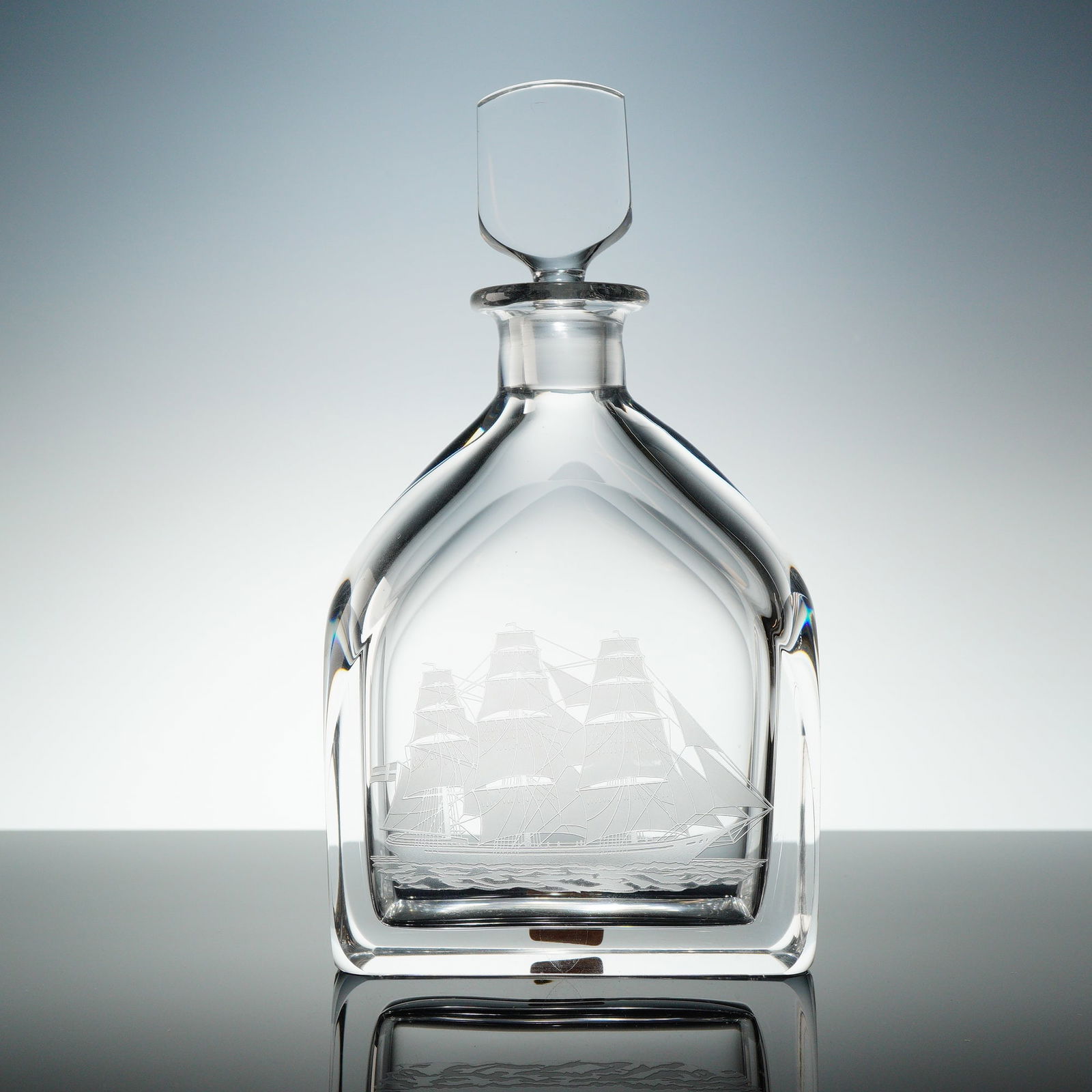 Orrefors Engraved Ship Motif Crystal Decanter with Stopper: A two-piece Orrefors crystal decanter set atributed to designer Edward Hald. The heavy, clear crystal decanter features a square body, sloped shoulders, and a narrow neck, executed in a clean, faceted
