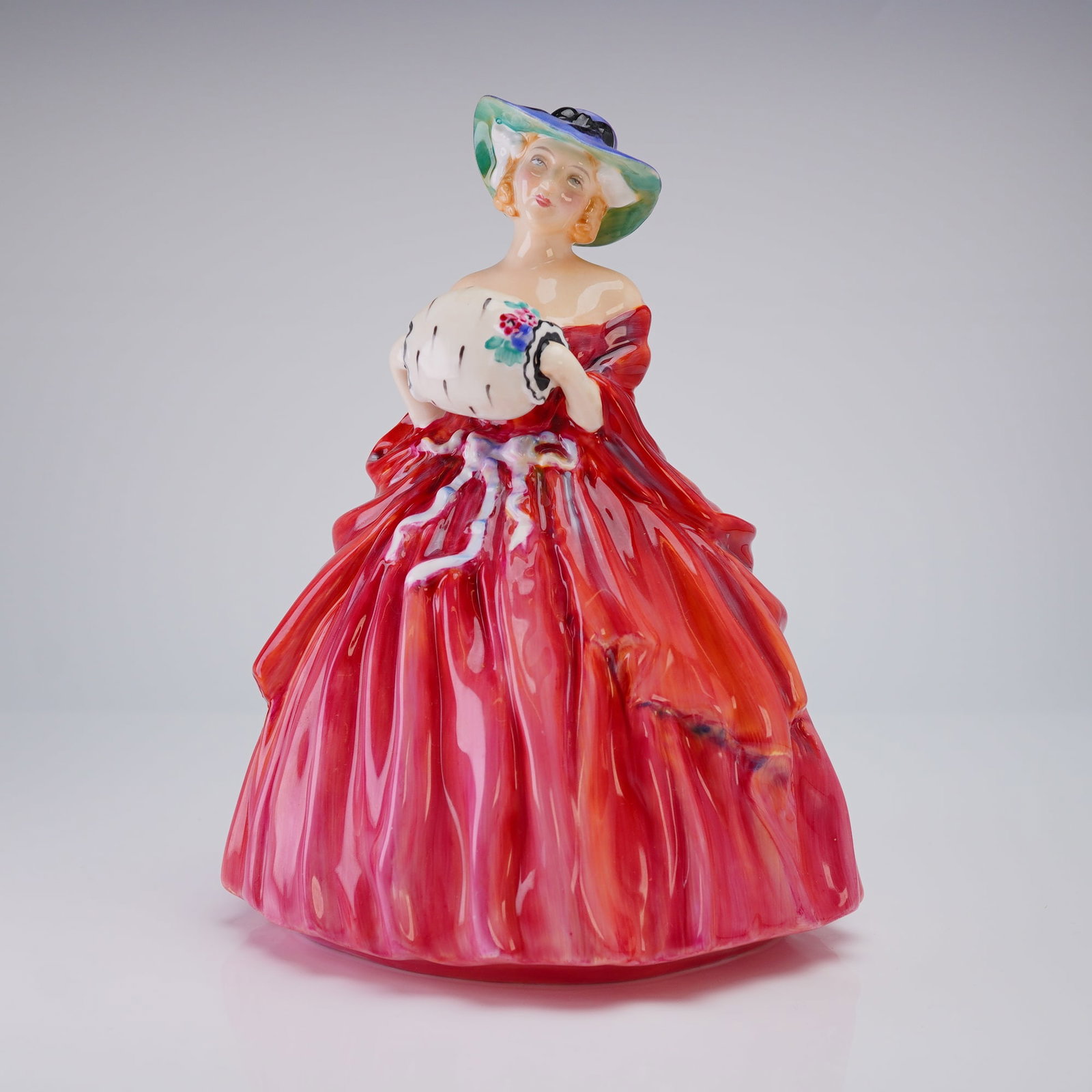 Royal Doulton Figurine Genevieve HN1962: A Royal Doulton porcelain figurine, depicting a woman in a red dress and blue/green hat holding a white fur muff, marked on the base with the model number and backstamp. Dimensions: 5.75"L x 5.25"W x