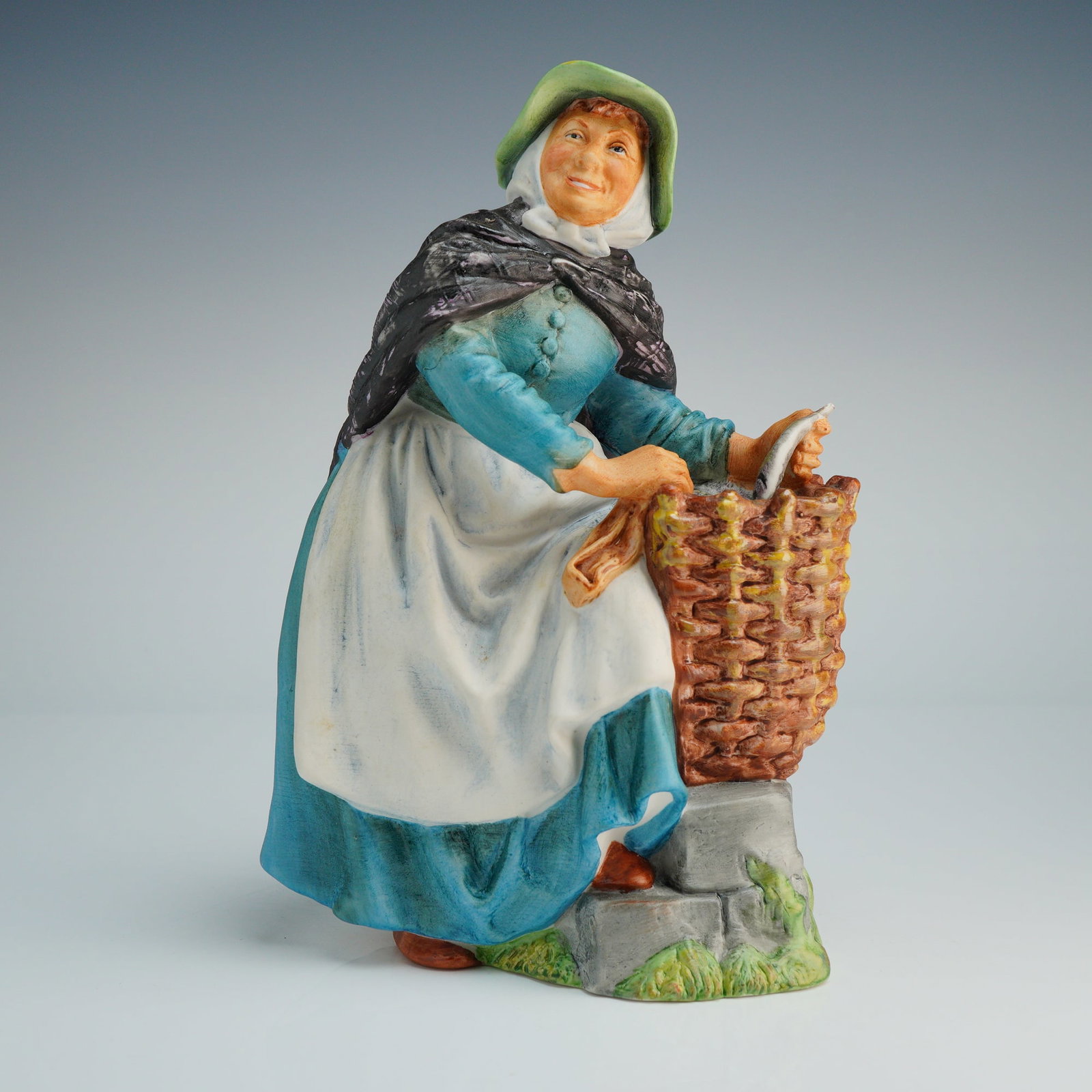 Royal Doulton Figurine Old Meg HN2494: A Royal Doulton hand-painted porcelain figurine titled Old Meg, model number HN 2494. The piece depicts an elderly woman in traditional attire, including a green bonnet, a white headscarf, a textured