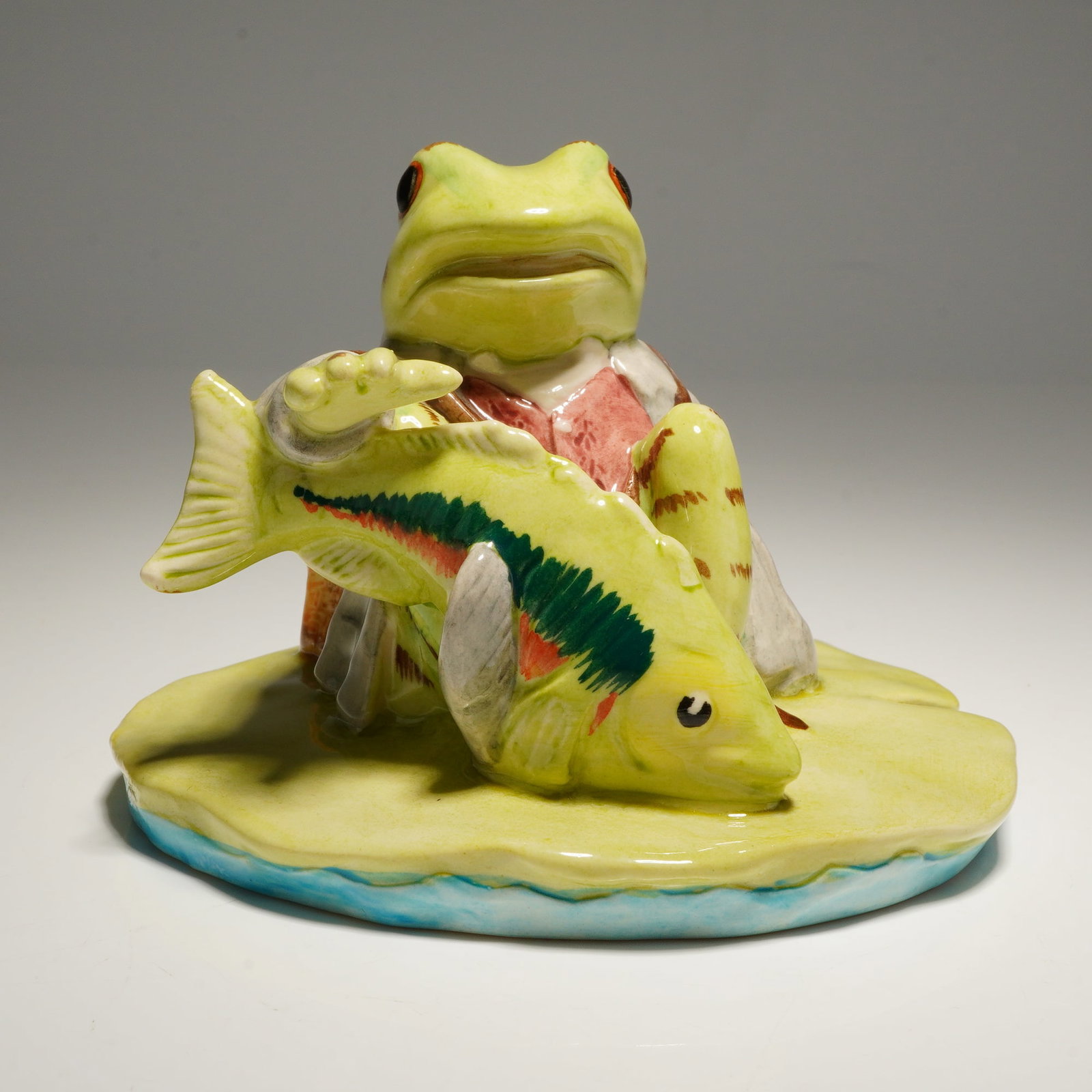 Beswick Beatrix Potter's Figurine, Jeremy Fisher Catches a Fish: Model number P3919, depicts an anthropomorphic frog seated on a lily pad holding a large fish, with a short V-shaped cut in the lily pad. Beswick backstamp and marked Royal Doulton. Includes original