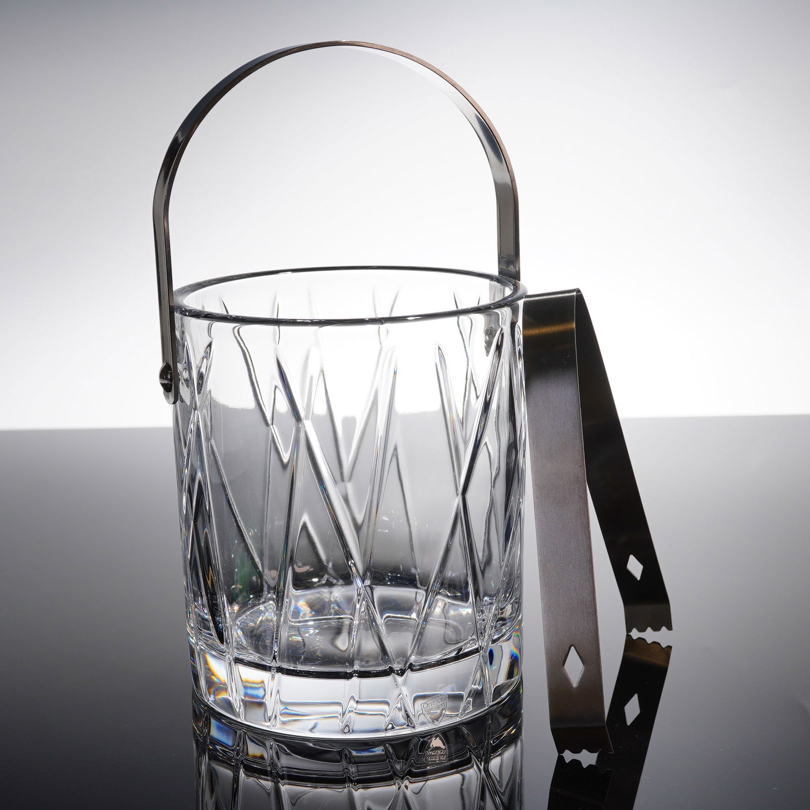 Orrefors City Crystal Ice Bucket and Tongs Set: A two-piece Orrefors City barware set consisting of a cut crystal ice bucket and associated metal tongs. The cylindrical ice bucket is executed in heavy clear crystal featuring deep faceted cutting in