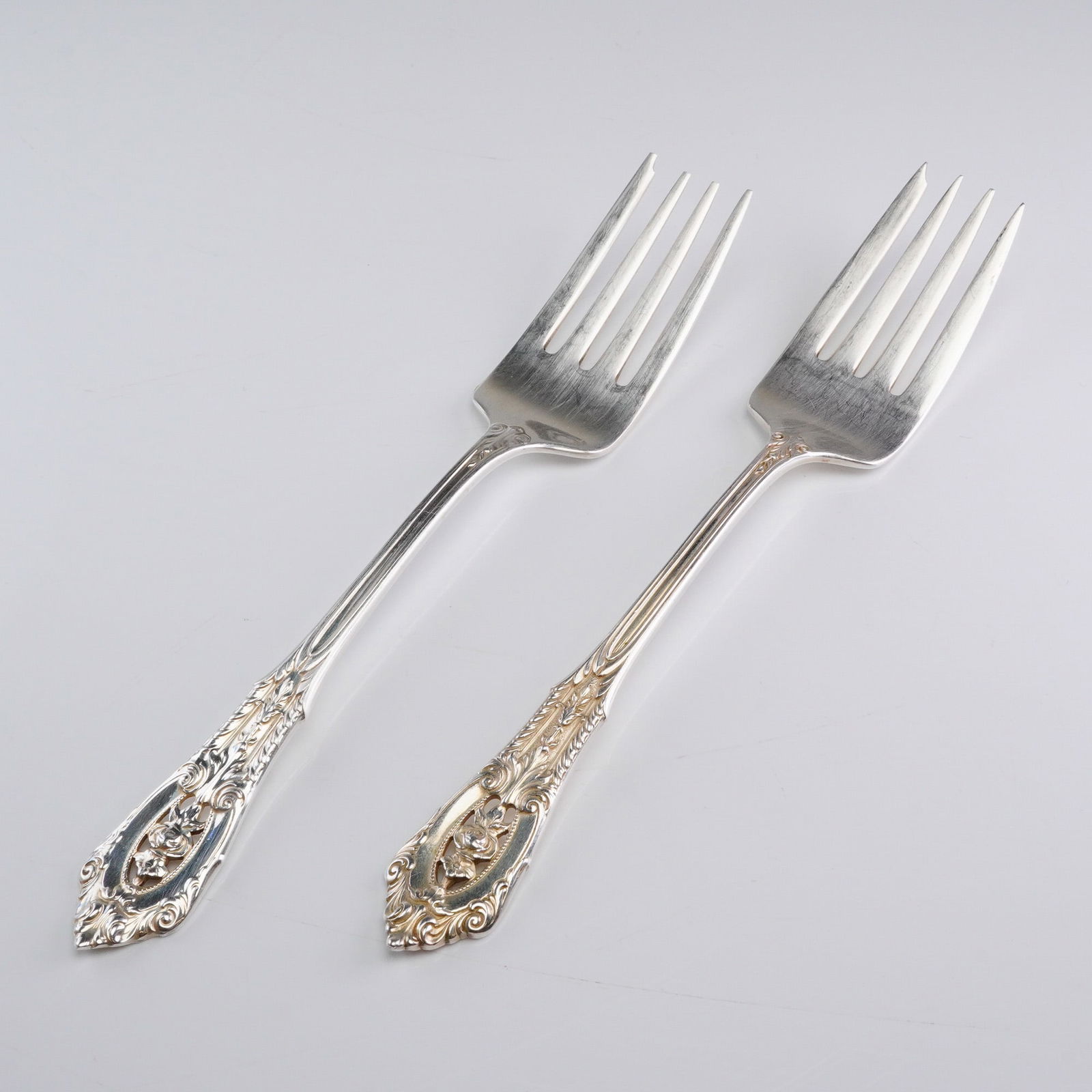 A Pair of Wallace Rose Point Sterling Silver Salad Forks: A 2pc set of Wallace sterling silver forks in the 'Rose Point' pattern. These are salad forks featuring an ornate, heavily decorated handle design typical of American Revivalist flatware. The decorati