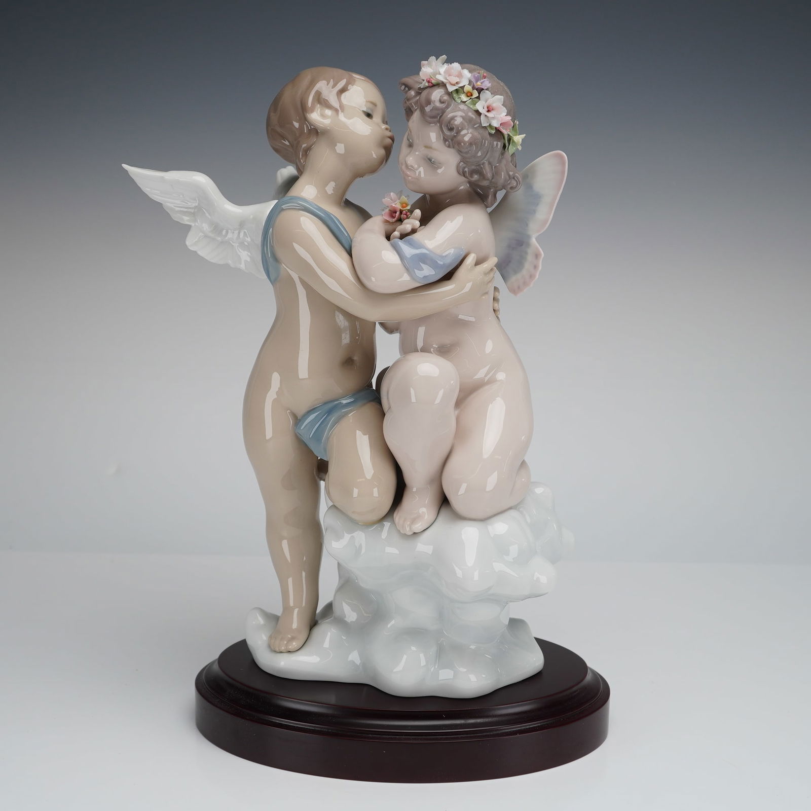 Lladro Heaven and Earth Porcelain Figurine 1824 with Base, Signed: A glazed porcelain figural group manufactured by Lladro, titled "Heaven and Earth" (Besos en el Cielo). The sculpture depicts two embracing putti (cherubs) standing upon a white cloud formation. The f