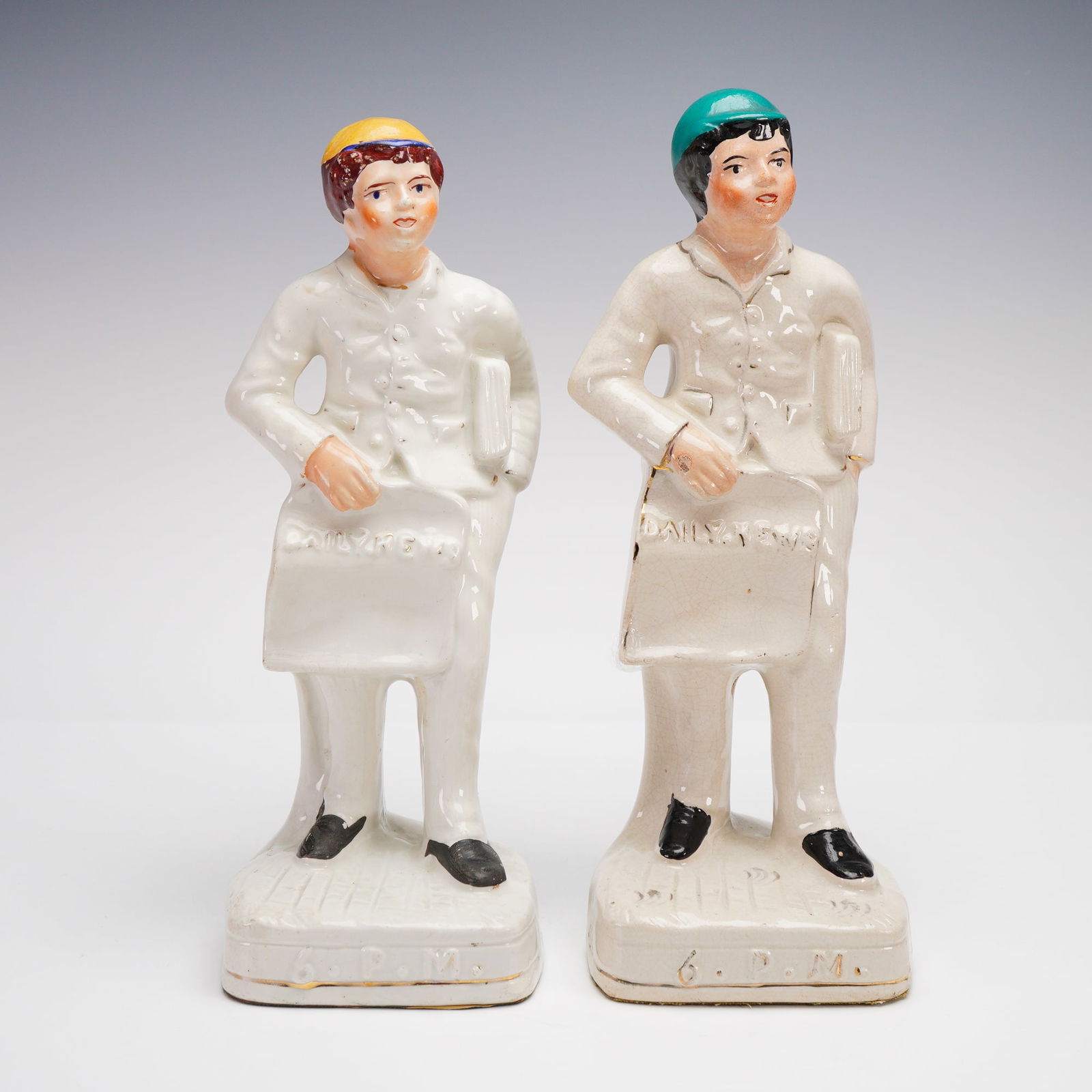 2pc Antique Staffordshire Sculptures , Daily News 6PM: Victorian-era Staffordshire porcelain figurines depicting young newspaper delivery boys, each holding a "Daily News" bag marked 6 P.M. at the base. These figures, commonly attributed to Staffordshire