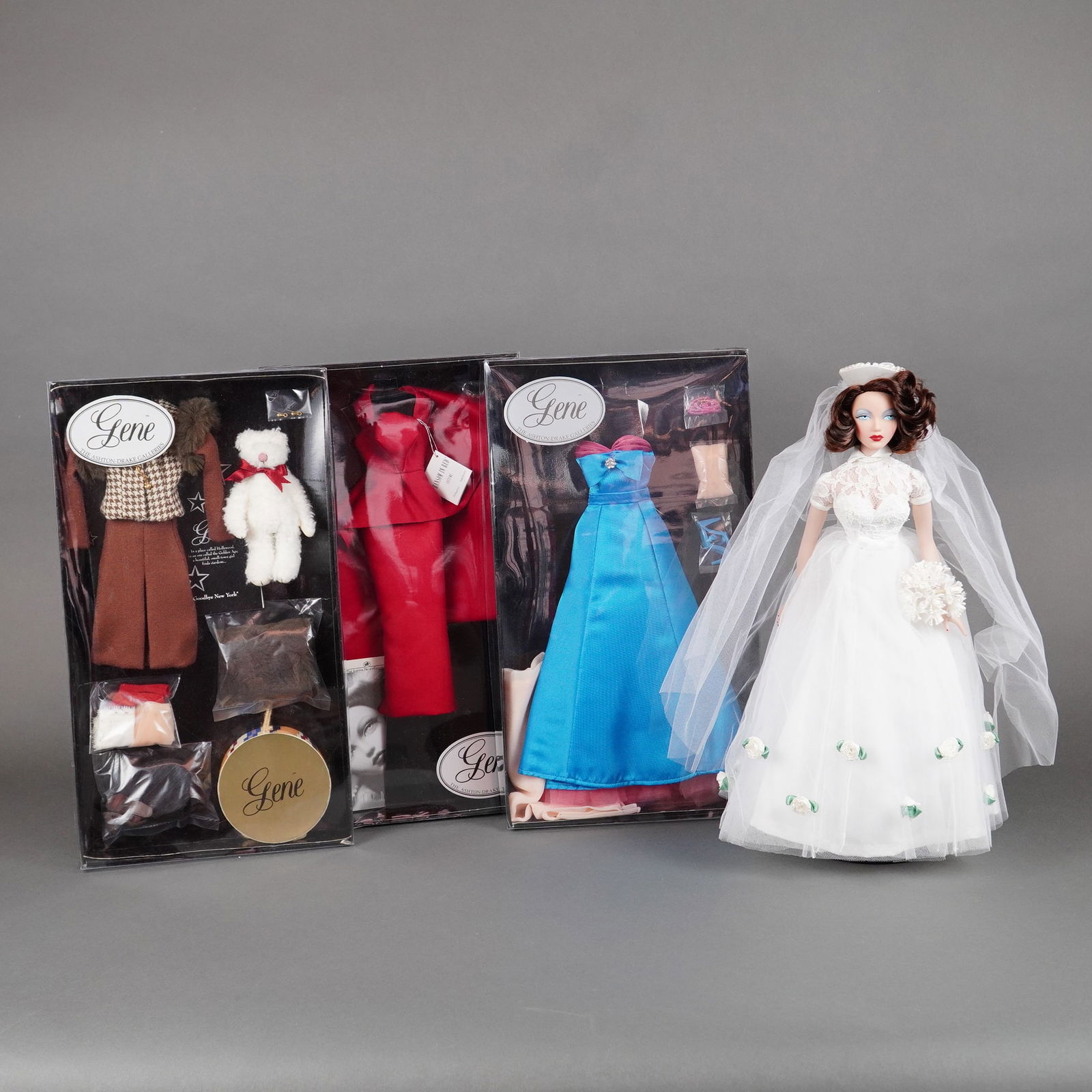 4pc Gene Marshall Monaco Bride by Ashton-Drake w/ Outfits & COA: A collection of four collectible items from the Ashton-Drake Galleries Gene Marshall series, designed by Mel Odom, centered around the "Gene in Monaco Bride" doll. The main doll features brown rooted