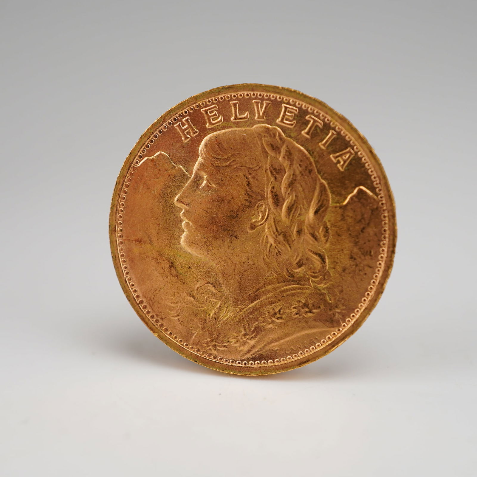 1947-B 20 Francs Swiss Vreneli Helvetia Gold Coin: Struck at the Bern Mint, Switzerland. Featuring a detailed obverse with the bust of a young woman from Oberhasli facing left, adorned with flowing tresses and a garland of edelweiss against a mountain