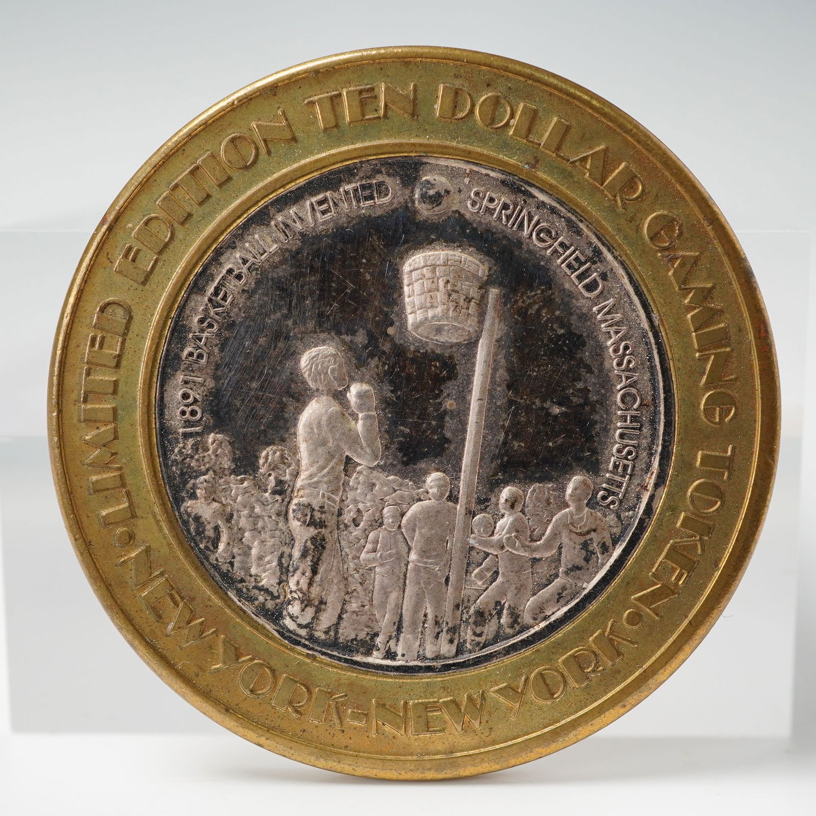 New York-New York Hotel & Casino Limited Edition Ten Dollar Gaming Token: The center strike is fine silver, surrounded by a brass outer ring. The obverse features an early basketball scene commemorating the 1891 invention of the sport in Springfield, Massachusetts, encircle