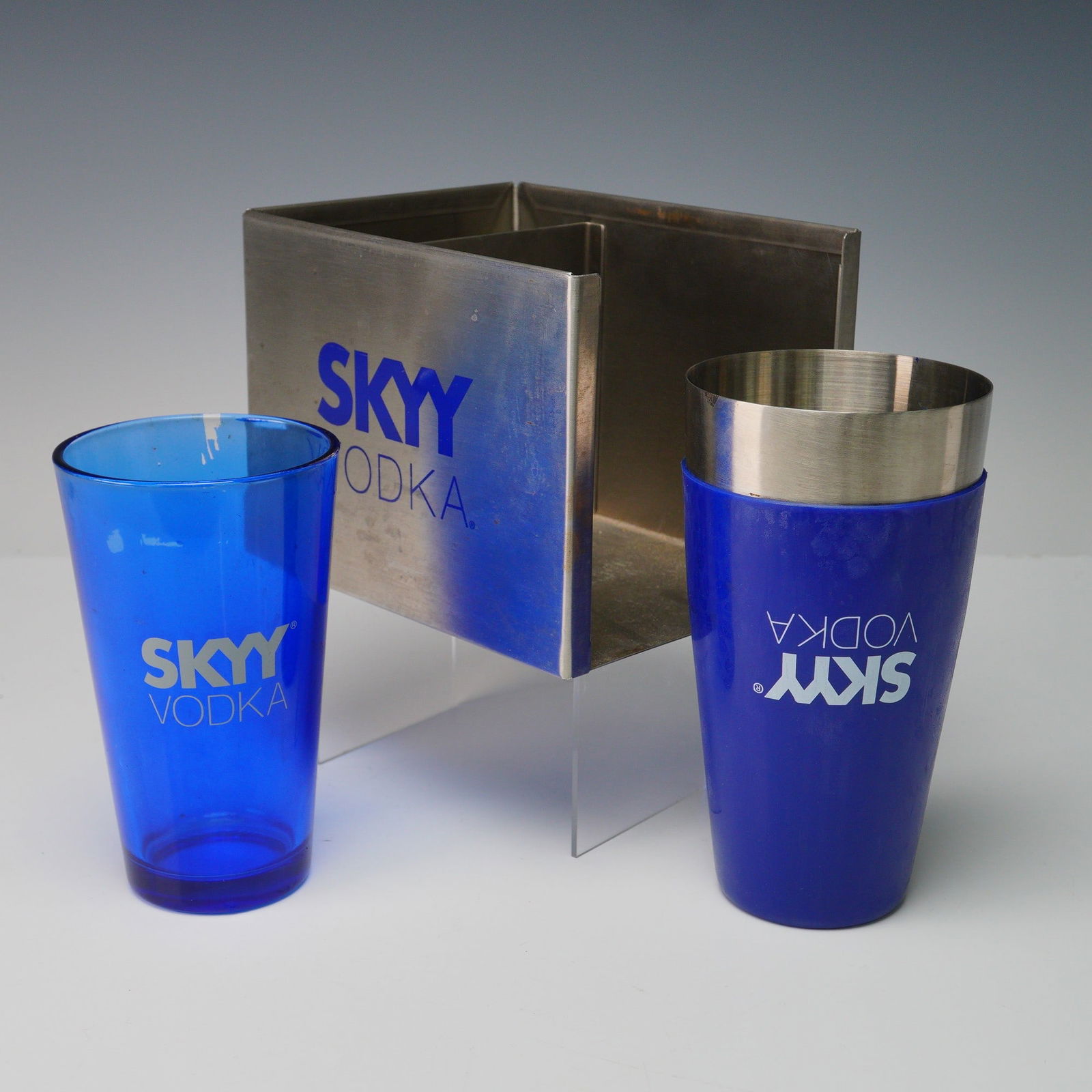 3pc Skyy Vodka Promotional Stainless Steel Bar Set: A promotional 3 piece barware set including a cobalt blue mixing glass, a coordinating shaker tin, and a brushed metal bar caddy, each prominently branded with the iconic SKYY Vodka logo in white or b