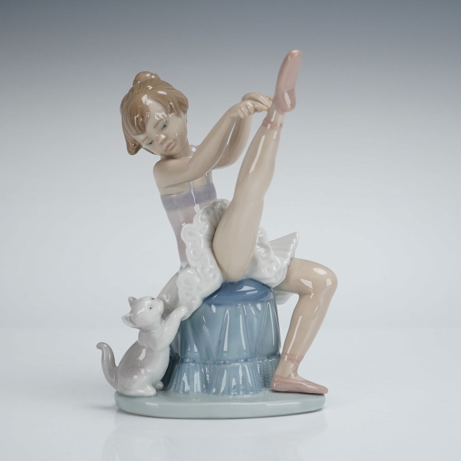 Lladro Porcelain Figurine Tuesdays Child 6014: A Lladro Porcelain Figurine, model number 6014, titled "Tuesday's Child" (Nina martes). The glossy glazed figurine depicts a young ballet dancer seated on a ruffled blue stool, adjusting a pink
