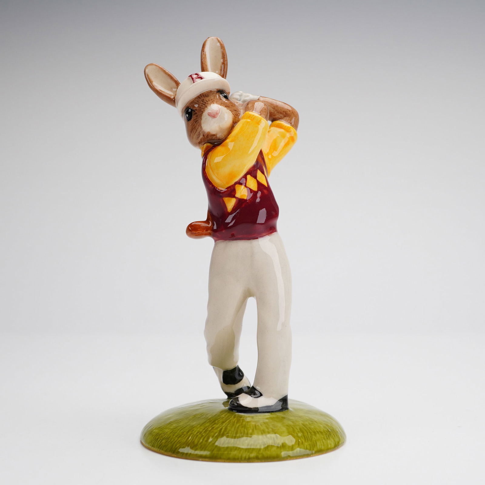 Royal Doulton Bunnykins Figurine, Golfer DB255: A charming Royal Doulton Bunnykins figurine depicting a golfing rabbit mid-swing. Handcrafted and hand-decorated, this piece is part of the Bunnykins collection, renowned for its whimsical and collect