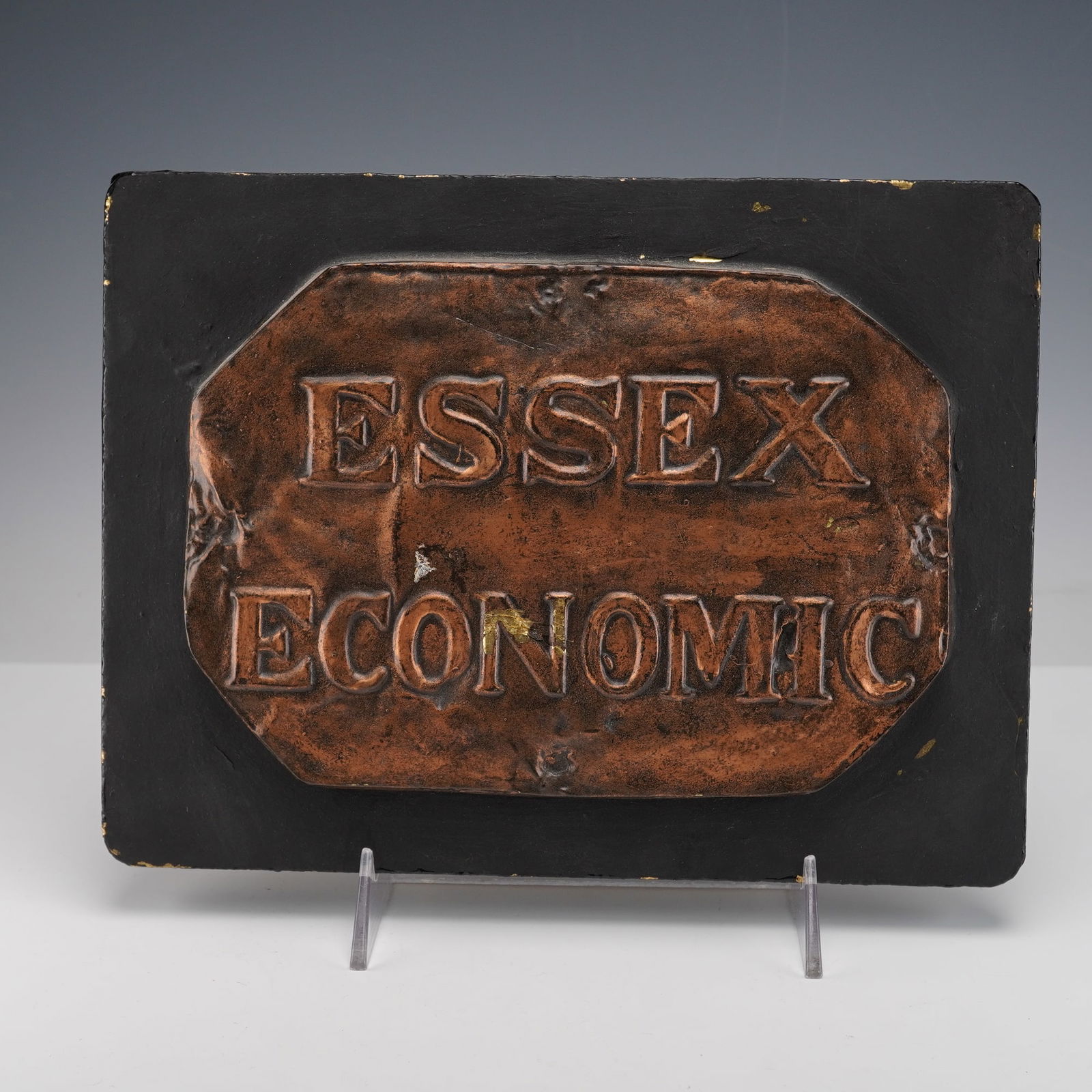 Essex Economic Fire Office by E. V. Jackson Reproduction Fire Mark Plaque: This plaque shows a raised copper colored octagonal plate with Essex Economic in bold lettering on a black backing. The reverse has a label noting it is a reproduction molded from an original fire mar