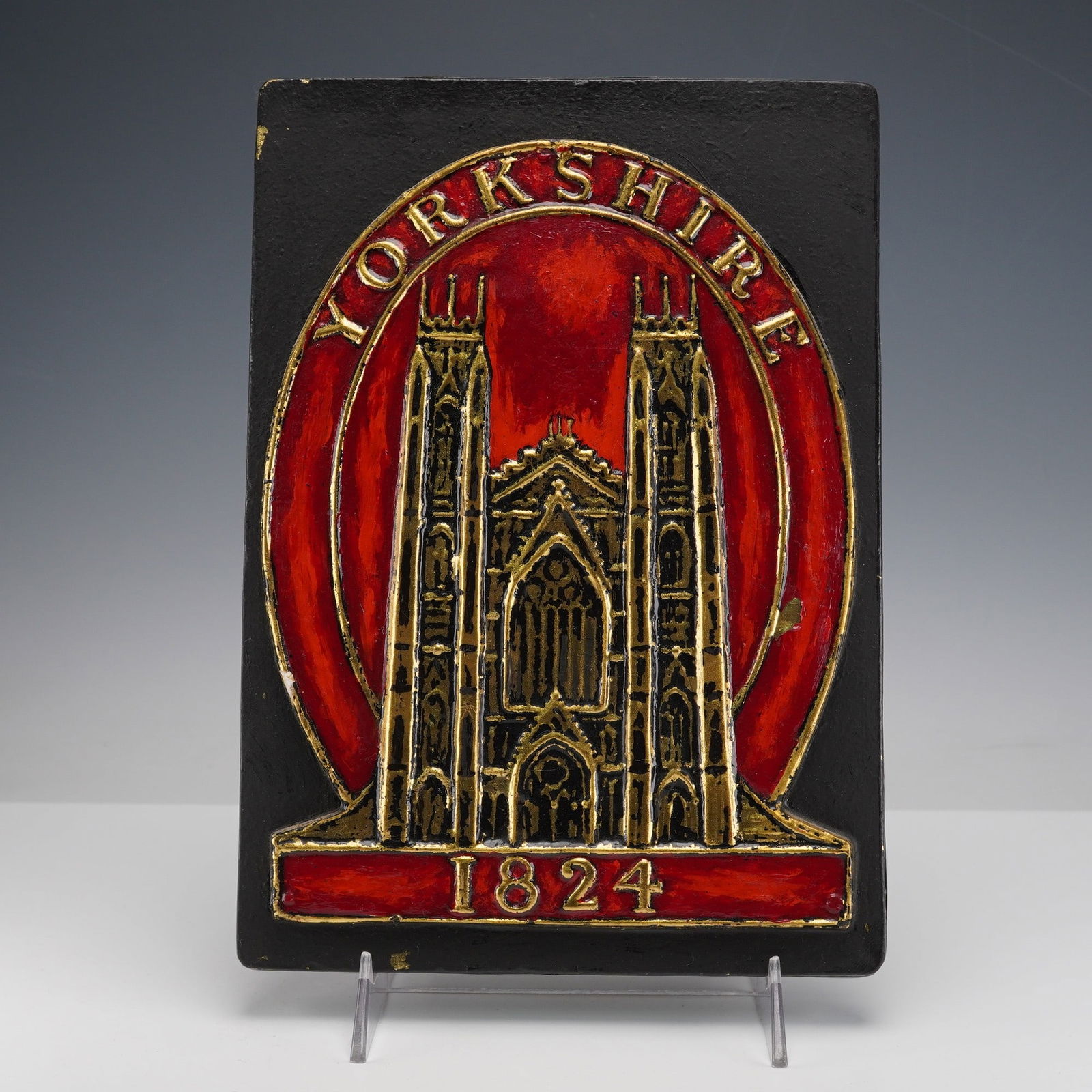 Yorkshire Assurance Company Fire Mark Plaque: his plaque shows a raised gold colored cathedral design against a bright red background with Yorkshire across the top and 1824 at the bottom. It is mounted on a black backing and has a label on the re