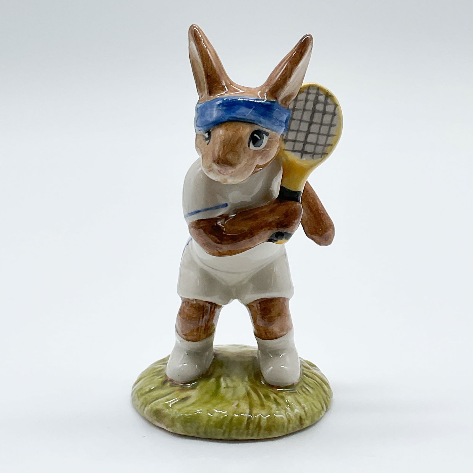 Ace Bunnykins DB42 - Royal Doulton Bunnykins: This charming Royal Doulton Bunnykins figurine, titled "Ace Bunnykins," features a rabbit dressed in tennis attire, complete with a racquet and a blue headband. Crafted from fine English porcelain,