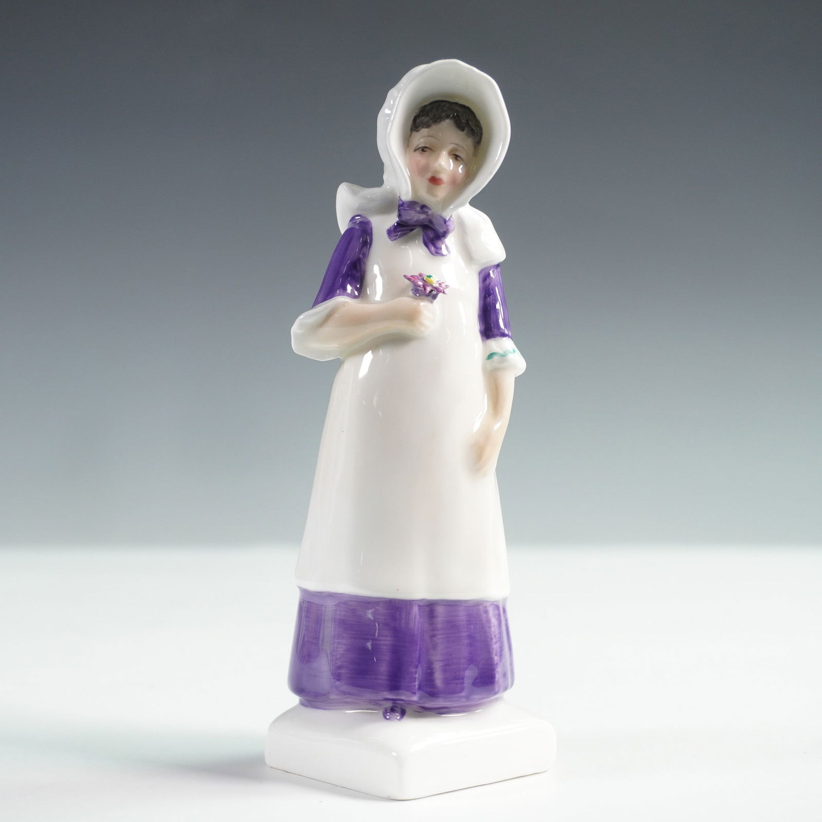 Anna HN2802 - Royal Doulton Figurine: Royal Doulton figurine titled Anna HN2802, depicting a young woman in a traditional bonnet and long purple dress accented with a white apron, holding a delicate bouquet. Designed by Peggy Davies and i