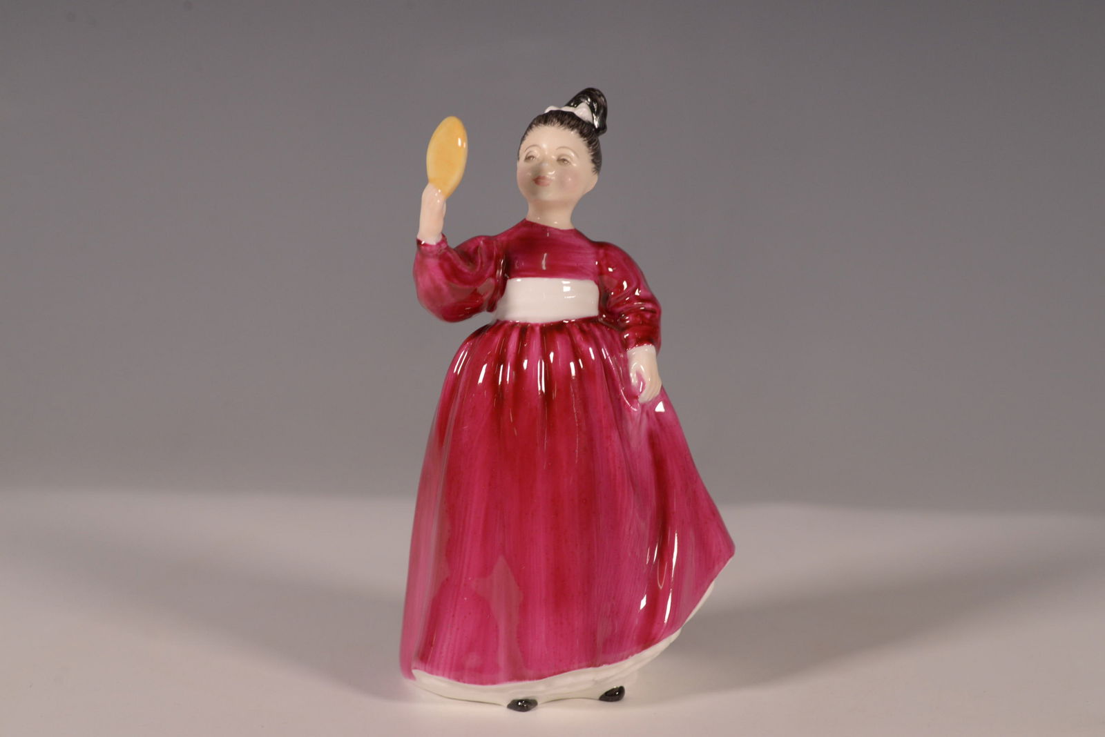 Royal Doulton Figurine Vanity HN2475: This charming Royal Doulton figurine, titled Vanity (HN2475), was issued in 1973 and retired in 1987. Crafted in fine bone china, it features a young woman in a flowing pink dress with a white sash, g