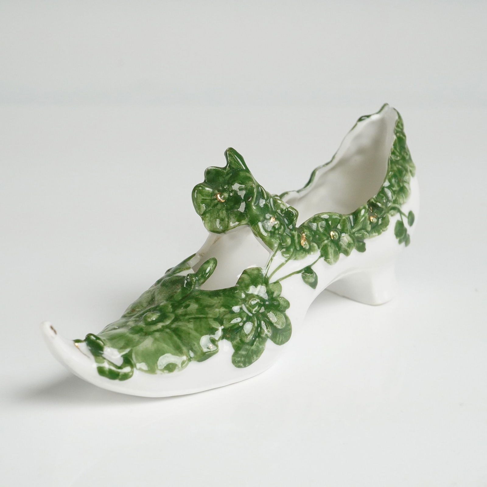 Porcelain Decorative Shoe Figurine with Green Floral Relief: A whimsical porcelain shoe figurine featuring a curled toe and raised heel, modeled after 18th-century footwear. The surface is richly adorned with green floral vines in high relief and accented with
