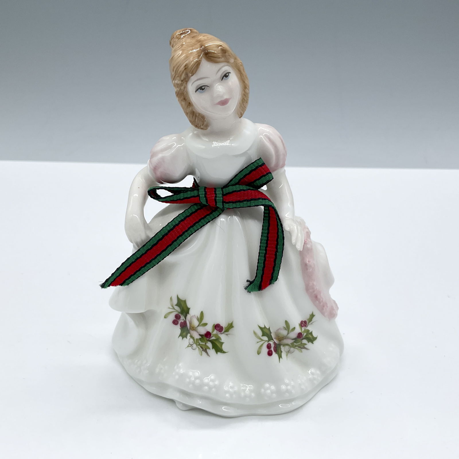 December - HN3329 - Royal Doulton Figurine: Glossy porcelain. Features a lovely girl in a white and pink dress decorated with Christmas flowers and a red and green ribbon. Royal Doulton backstamp. Issued: 20th century Dimensions: 3.75''L x 4''W