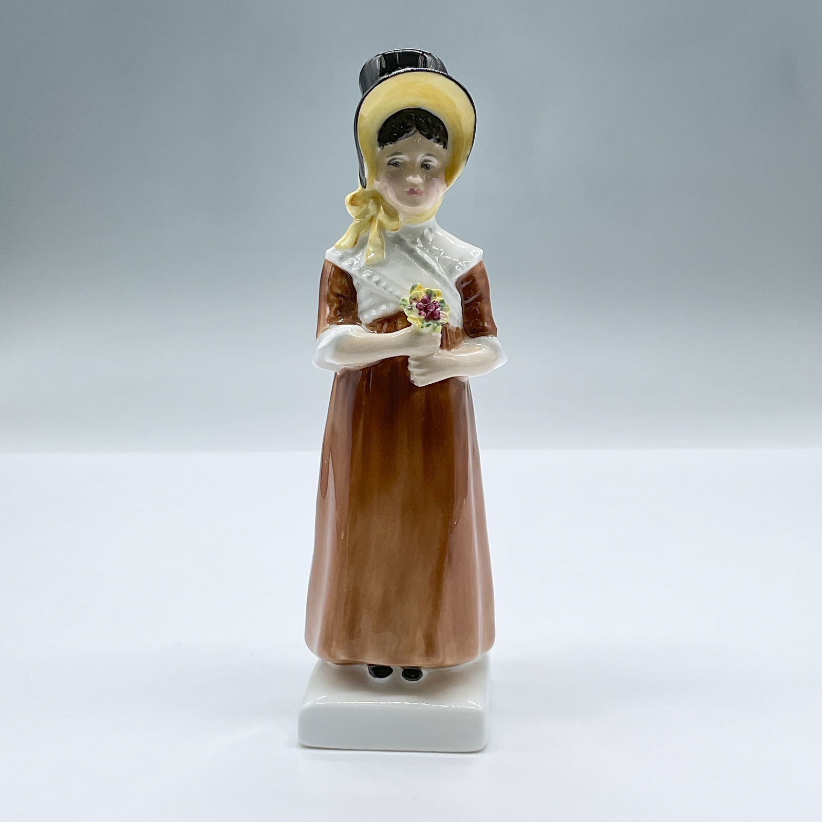 Louise HN2869 - Royal Doulton Figurine: The figure of a small girl in a brown dress and black and yellow hat, holding flowers. Part of the Kate Greenaway series. Royal Doulton backstamp. Artist: Peggy Davies Issued: 1979 - 1986 Dimensions: