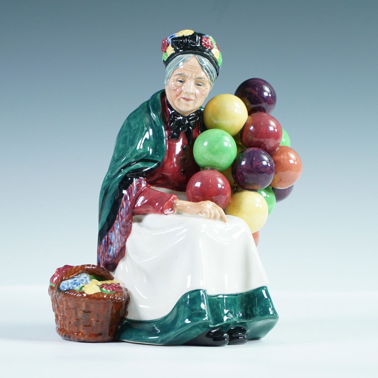 Royal Doulton Figurine, The Old Balloon Seller HN1315: Royal Doulton figurine titled The Old Balloon Seller, model HN1315. This hand-painted figure, introduced in 1929, depicts an elderly woman seated with a basket and colorful balloons, embodying one of