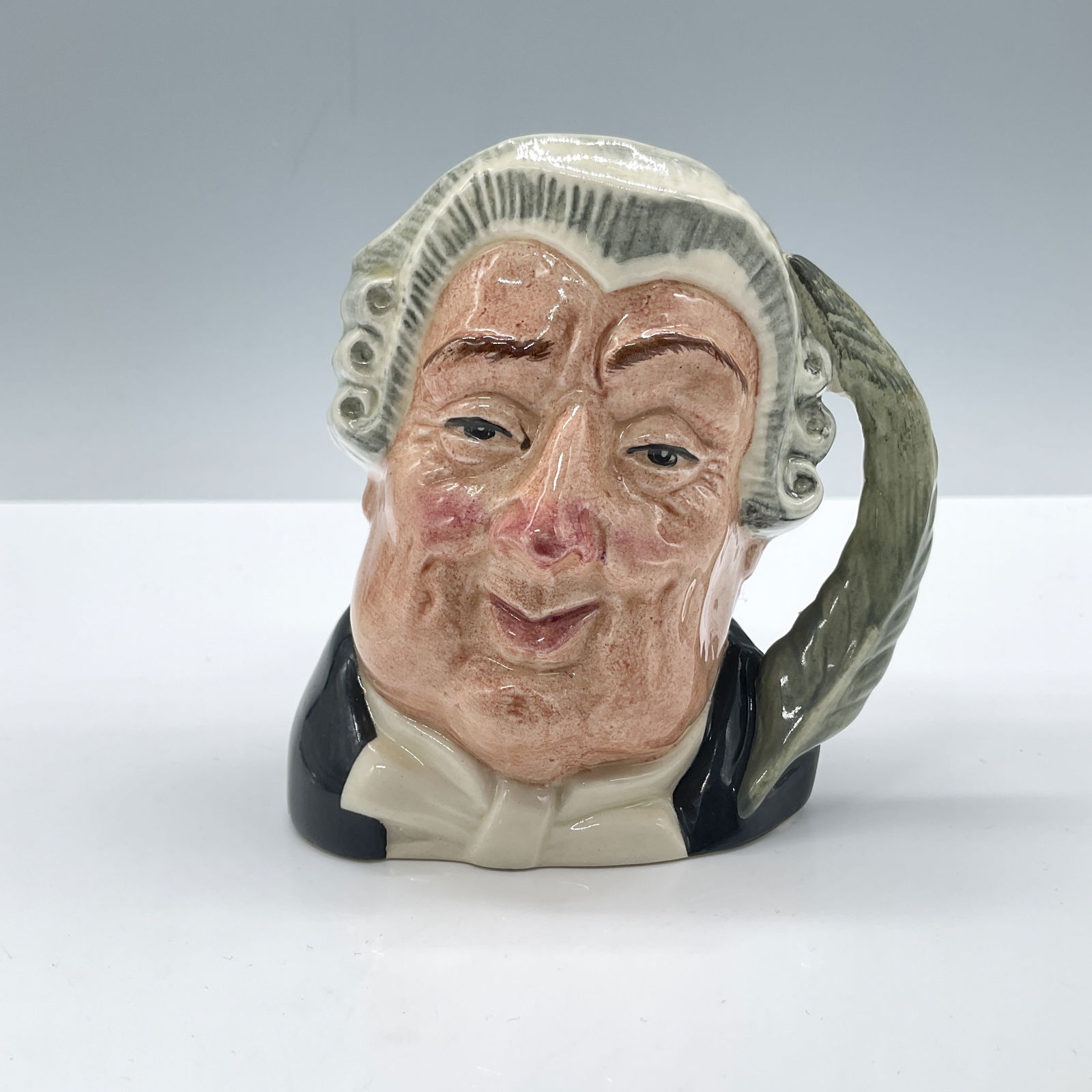 Lawyer D6504 - Small - Royal Doulton Character Jug: Glossy porcelain. Features black and white clothes with a feather handle. Royal Doulton Figurine. Artist: Max Henk Issued: 1959 - 1996 Dimensions: 2.75''L x 3.5''W x 3.75''H Country of Origin: England